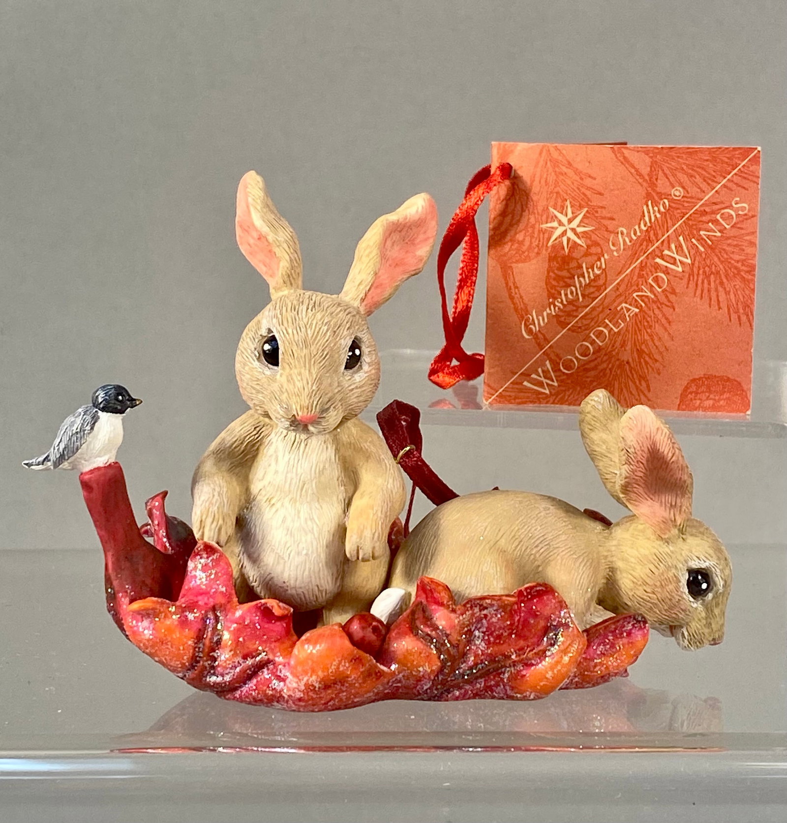 Radko Woodland Winds Bunny Drifter Ornament: Stand Not Included. Christopher Radko Woodland Winds Bunny Drifter holiday ornament. This piece is constructed of painted cast resin with detailed texturing to simulate fur and leaf veins. The