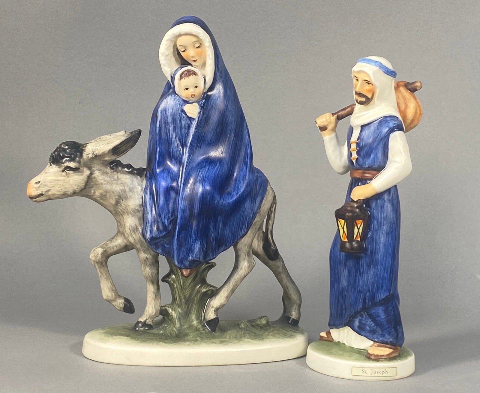 Two Goebel Porcelain Nativity Figurines Designed by Janet Robson: This lot features two glazed porcelain nativity-themed figurines produced by W. Goebel of West Germany and designed by artist Janet Robson. The first figurine, titled Flight into Egypt, depicts the