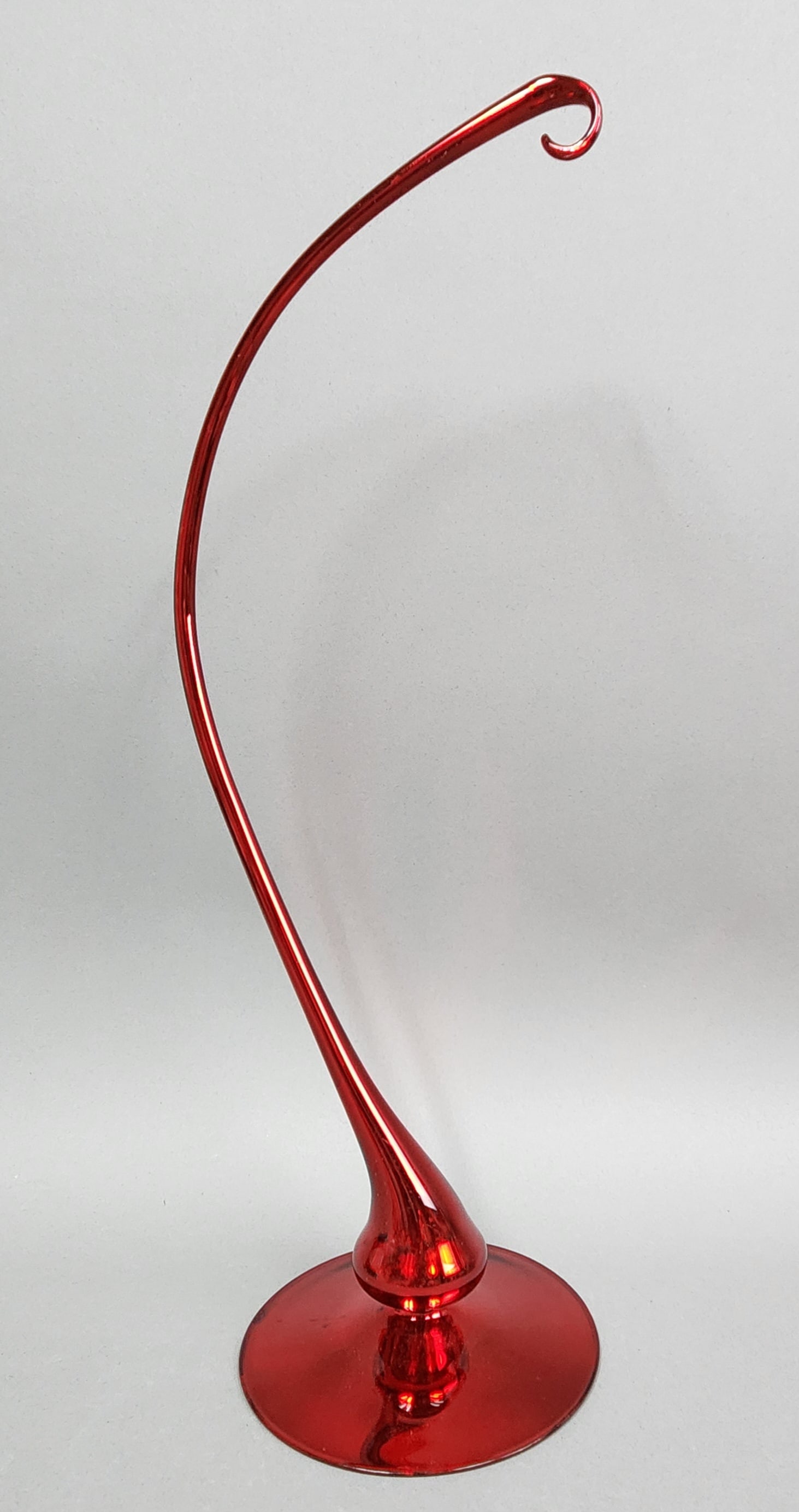 Large Radko Glass Ornament Stand: Christopher Radko tall, slender ornament stand crafted from red glass. Height: 19 inches. The internal silvered coating on the underside of the base shows flaking. The exterior red glass remains intac