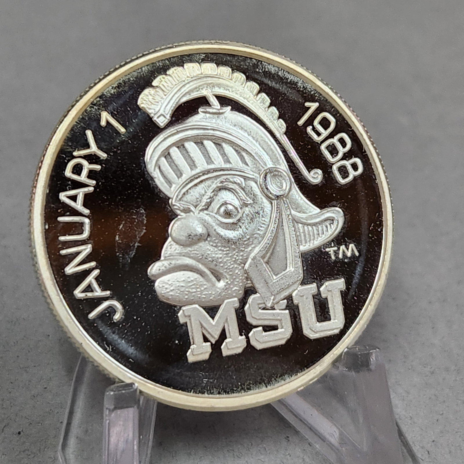 1988 MSU Rose Bowl Silver Coin 1 Troy Oz: A 1 troy ounce .999 fine silver commemorative round featuring the Michigan State University Spartan logo and Rose Bowl Pasadena Tournament of Roses design with edge-stamped serial number 02155. Excell