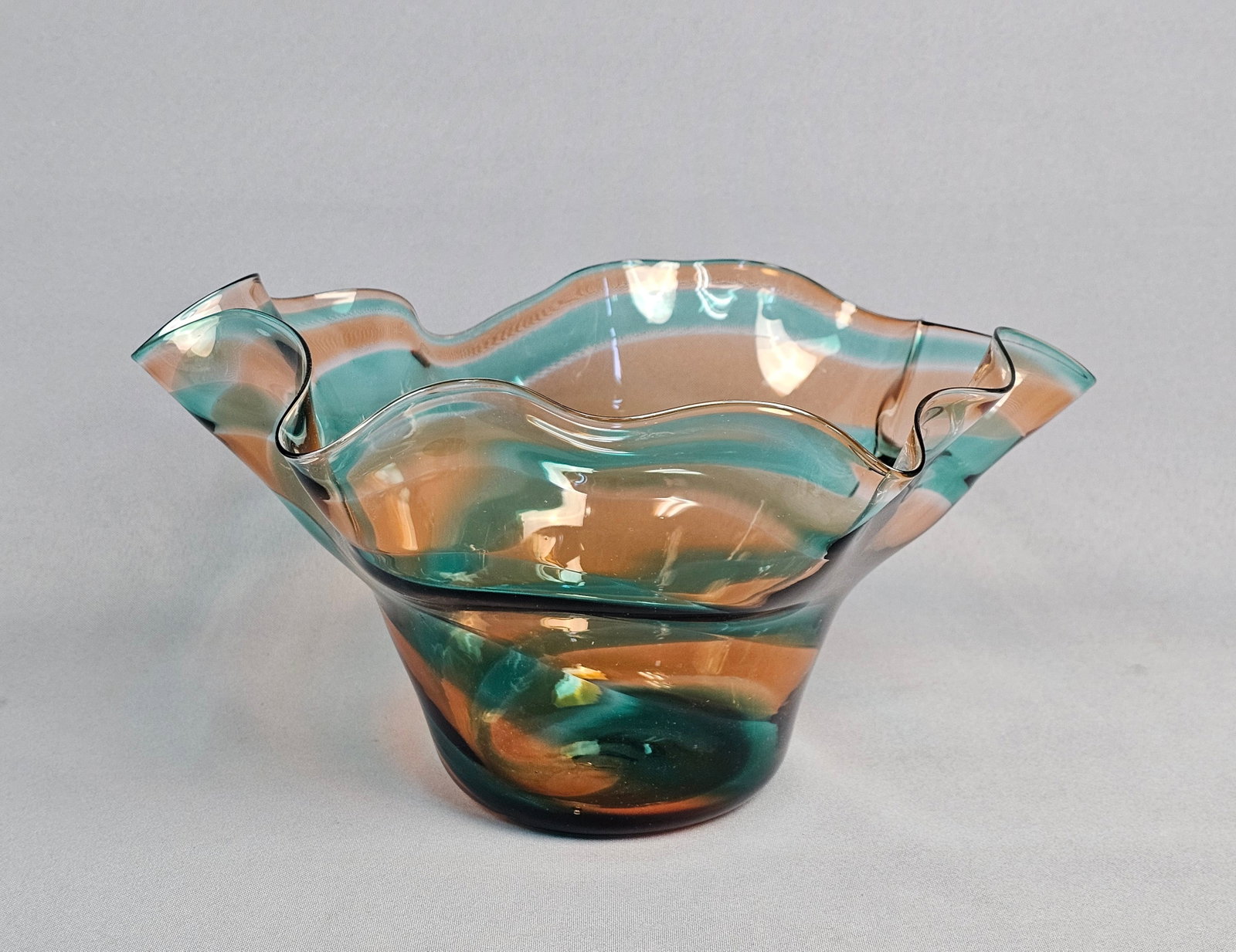 Signed Studio Art Glass Handkerchief Bowl: This hand-blown studio art glass bowl features a flared, undulating handkerchief-style rim. The vessel is decorated with internal spiraling bands of translucent teal-green and amber-peach colored glas