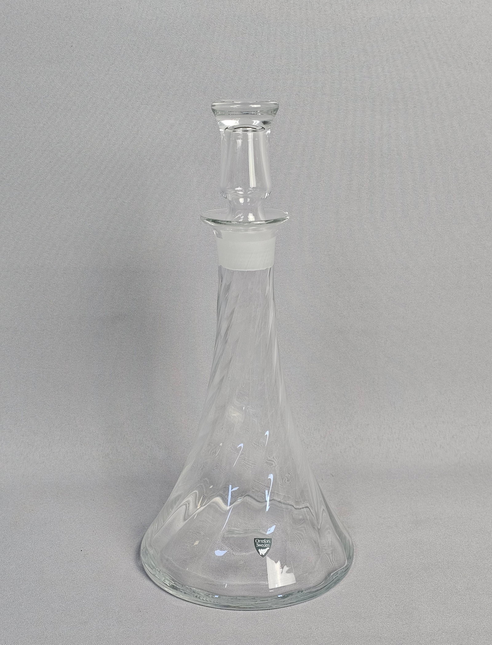 Orrefors Clear Crystal Decanter: A clear Swedish crystal decanter in the Helena pattern, designed by Gunnar Cyren for Orrefors. The piece features a tall, tapered conical body with a flared base, decorated with internal spiral optic 