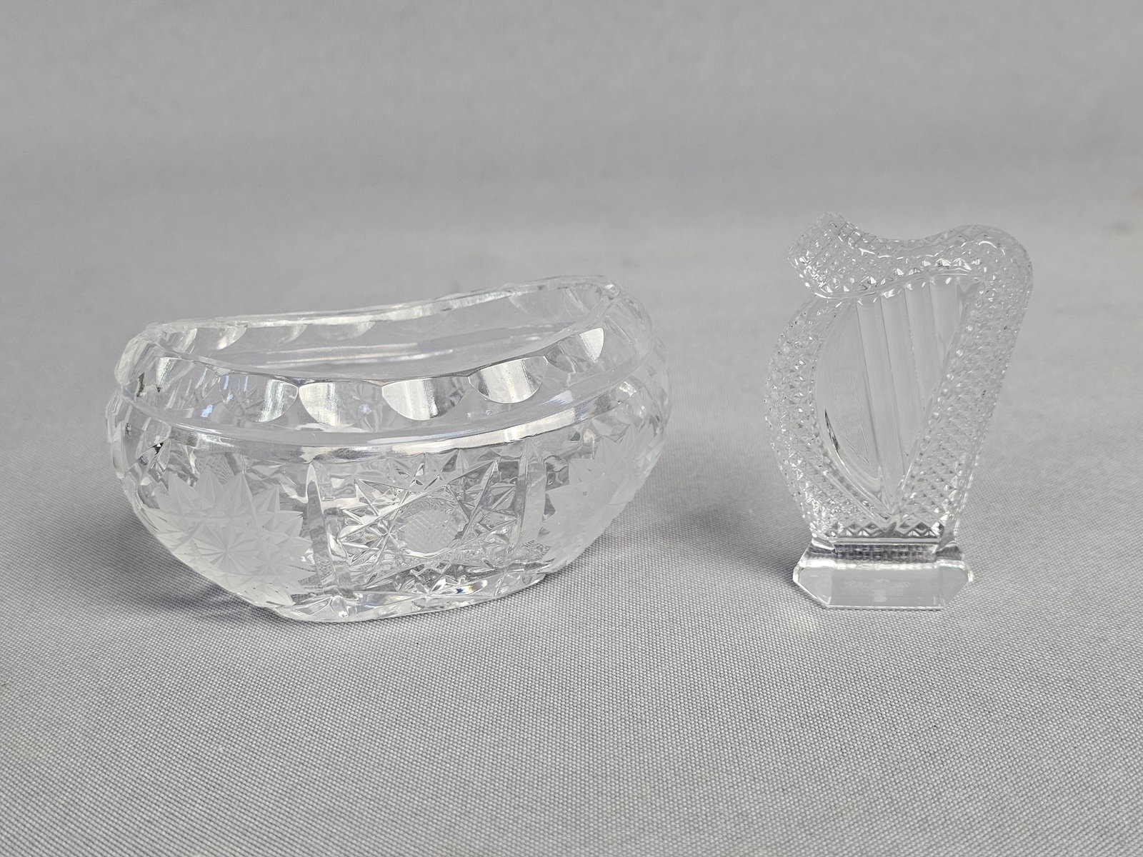 Two Pieces of Cut Crystal Including a Waterford Harp: This lot features two pieces of high-quality cut lead crystal. The first is a decorative harp figurine manufactured by Waterford Crystal. The second piece is an oval, boat-shaped dish featuring intric