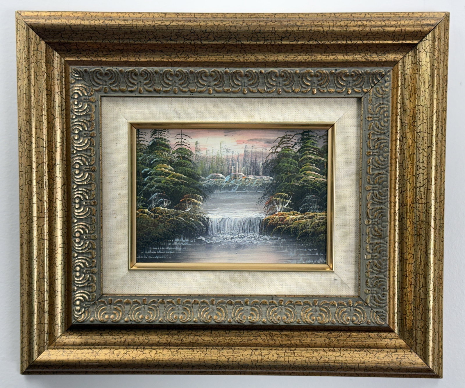 Waterfall Landscape Oil on Canvas: This oil on canvas board painting depicts a serene landscape featuring a waterfall cascading from an upper lake into a larger body of water below. The composition is flanked by dense evergreen trees w