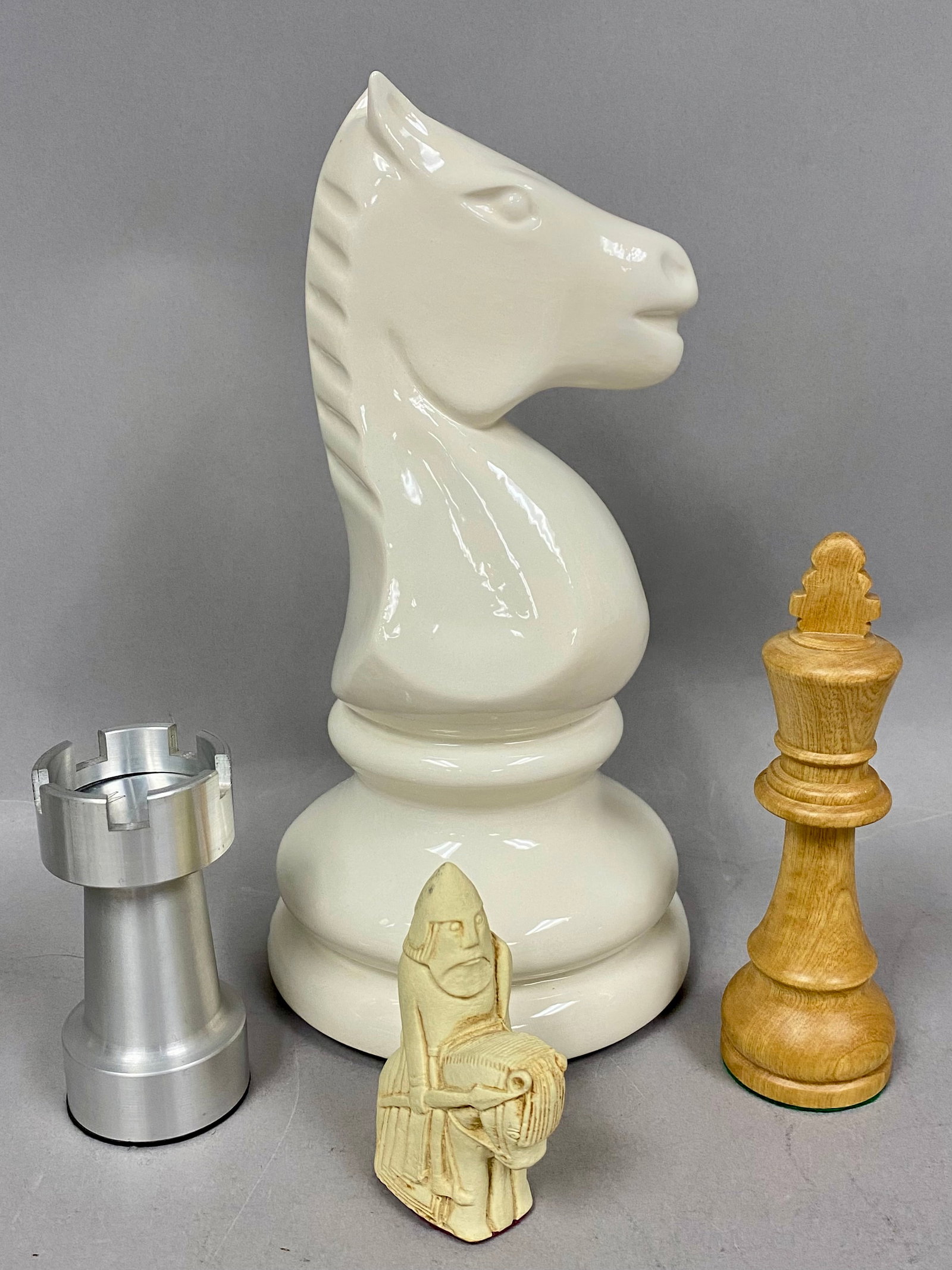 Decorative and Novelty Chess Pieces: A collection of various decorative and novelty chess pieces of differing styles, materials, and sizes. The group includes a large, glossy white-glazed ceramic knight featuring a hand-written mark on t