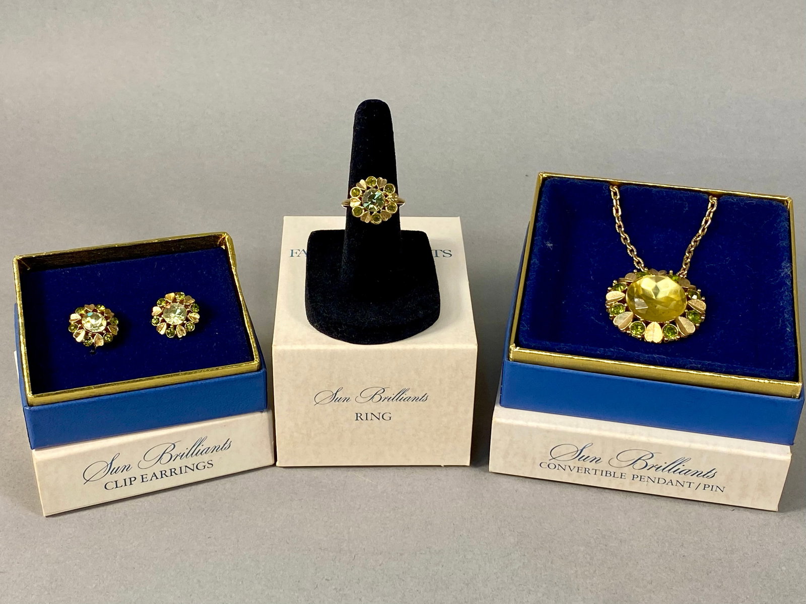 Vintage 1974 Avon Sun Brilliants Jewelry Set: A vintage Avon Sun Brilliants jewelry set, produced circa 1974. The collection includes a convertible pendant/brooch with a coordinating gold-tone chain, a pair of clip-on earrings, and ring. Each pie