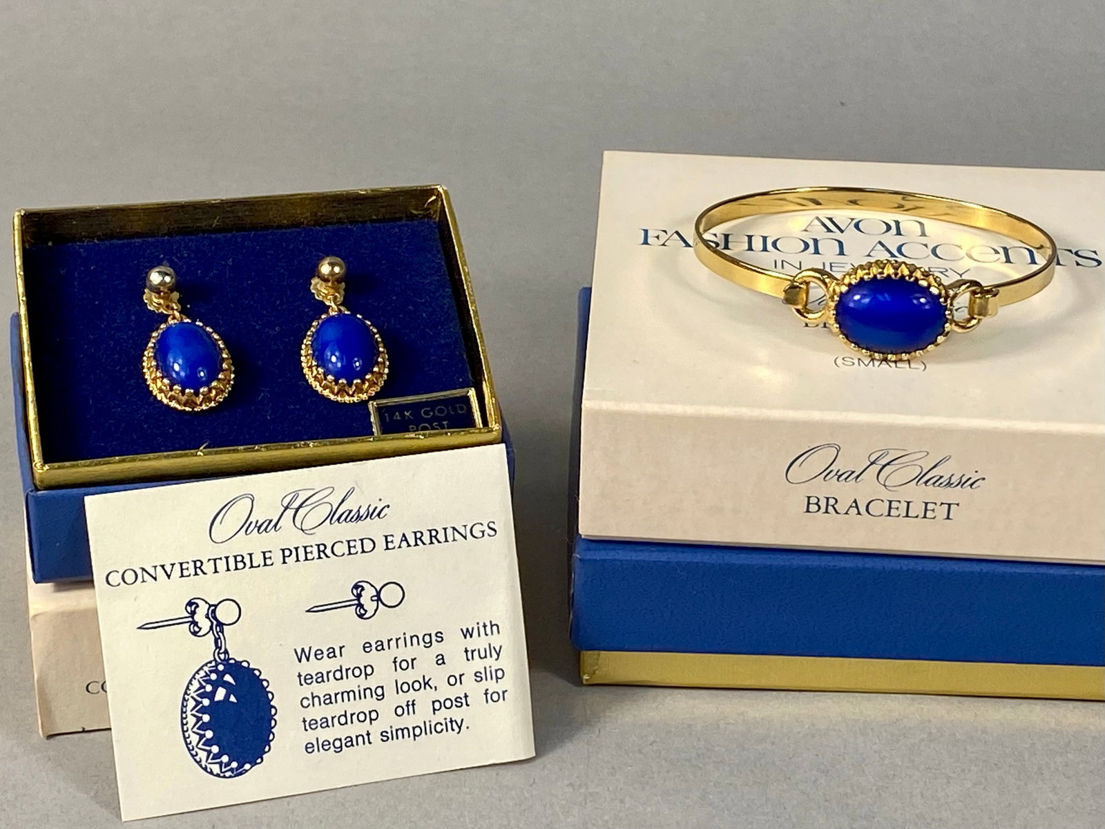 Avon 1974 Oval Classic Bangle Bracelet & Earrings: Avon Oval Classic jewelry set including a hinged bangle bracelet and a pair of convertible pierced earrings, dated 1974. Constructed from yellow gold-tone metal, the set features oval cobalt-blue cabo