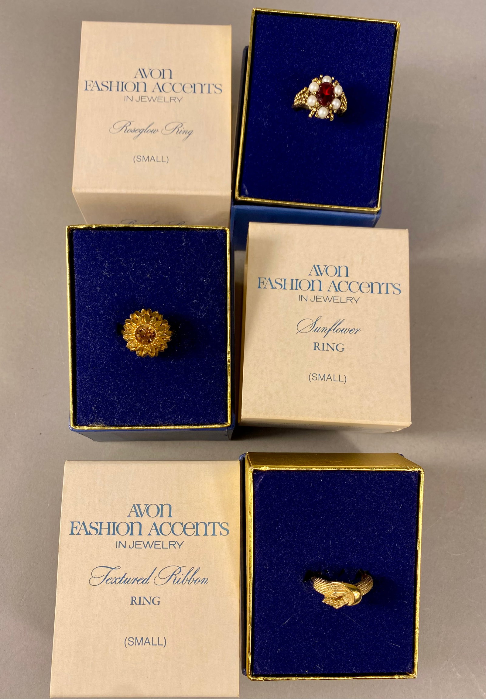 Three Vintage Avon Fashion Accents Gold-Tone Rings: A trio of vintage Avon Fashion Accents collection costume jewelry rings, each accompanied by its original blue velvet-lined presentation box and white cardboard outer sleeve. The collection includes a
