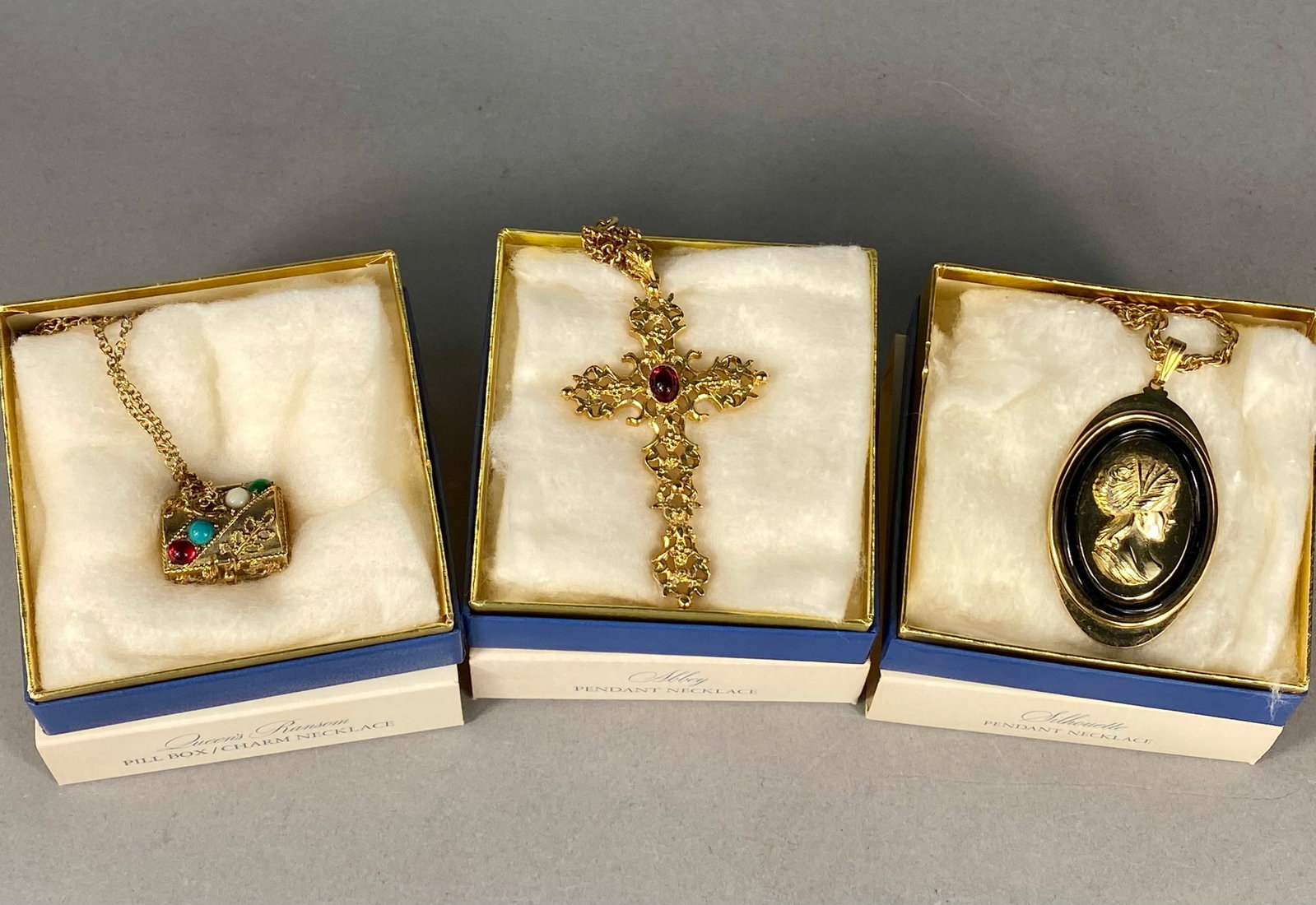 Three Vintage Avon Fashion Accents Pendant Necklaces: A trio of vintage Avon Fashion Accents in Jewelry pendant necklaces, each housed in its original retail box. The collection includes the Queens Ransom pill box and charm necklace dated 1974, the Abbey