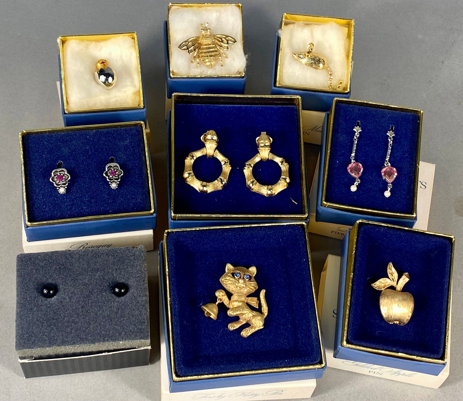 Nine Boxed Avon Vintage Costume Jewelry Sets and Pins: A collection of nine vintage Avon costume jewelry sets and novelty pins, dated between 1972 and 1994. Most items are presented in their original blue and white boxes. The collection consists of a Fris
