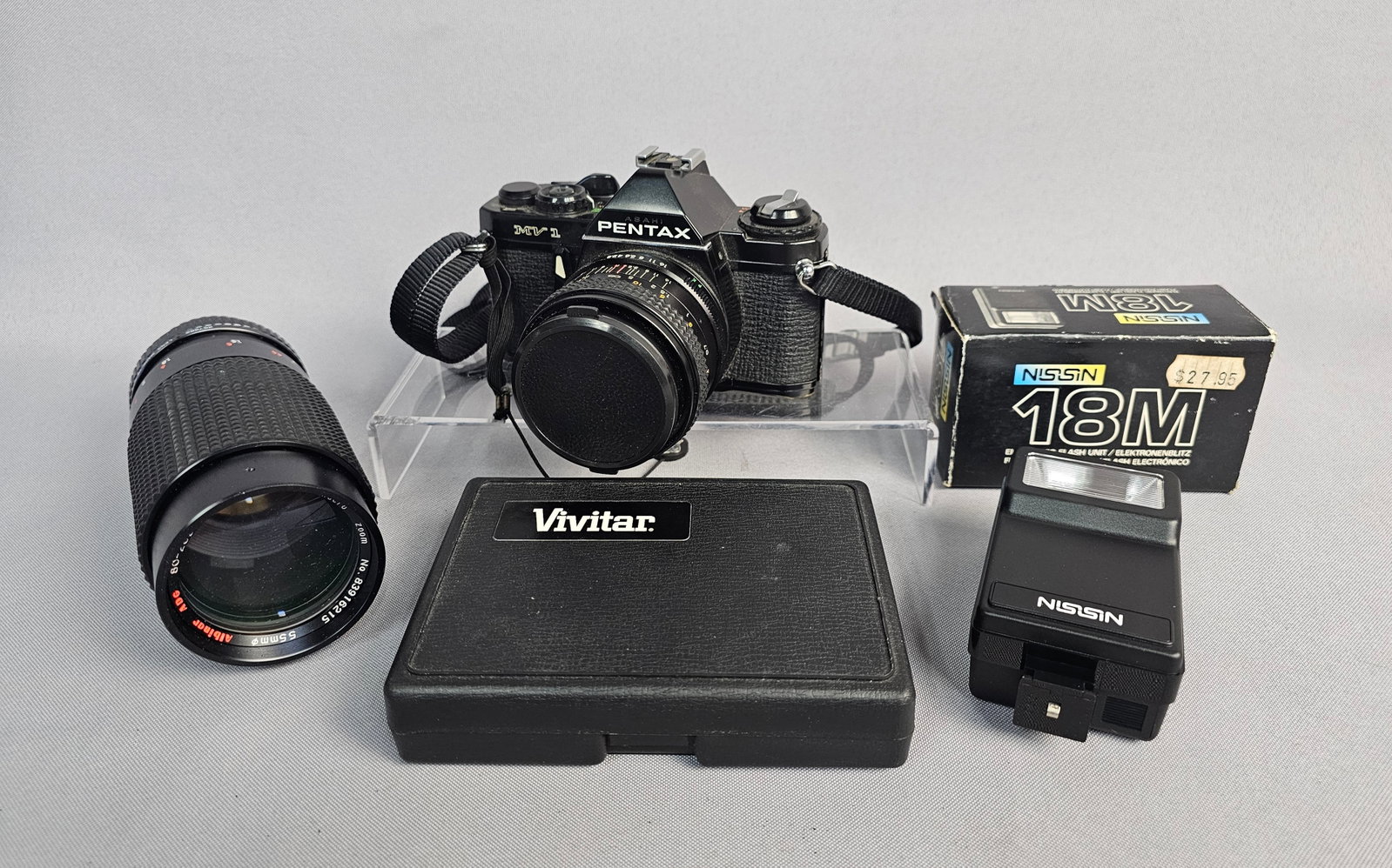 Pentax Camera with Two Lenses, Flash, and Accessories: An Asahi Pentax MV1 35mm single-lens reflex (SLR) film camera system. The camera body is constructed from polycarbonate and metal with a black finish and bears serial number 1736053 on the baseplate. 