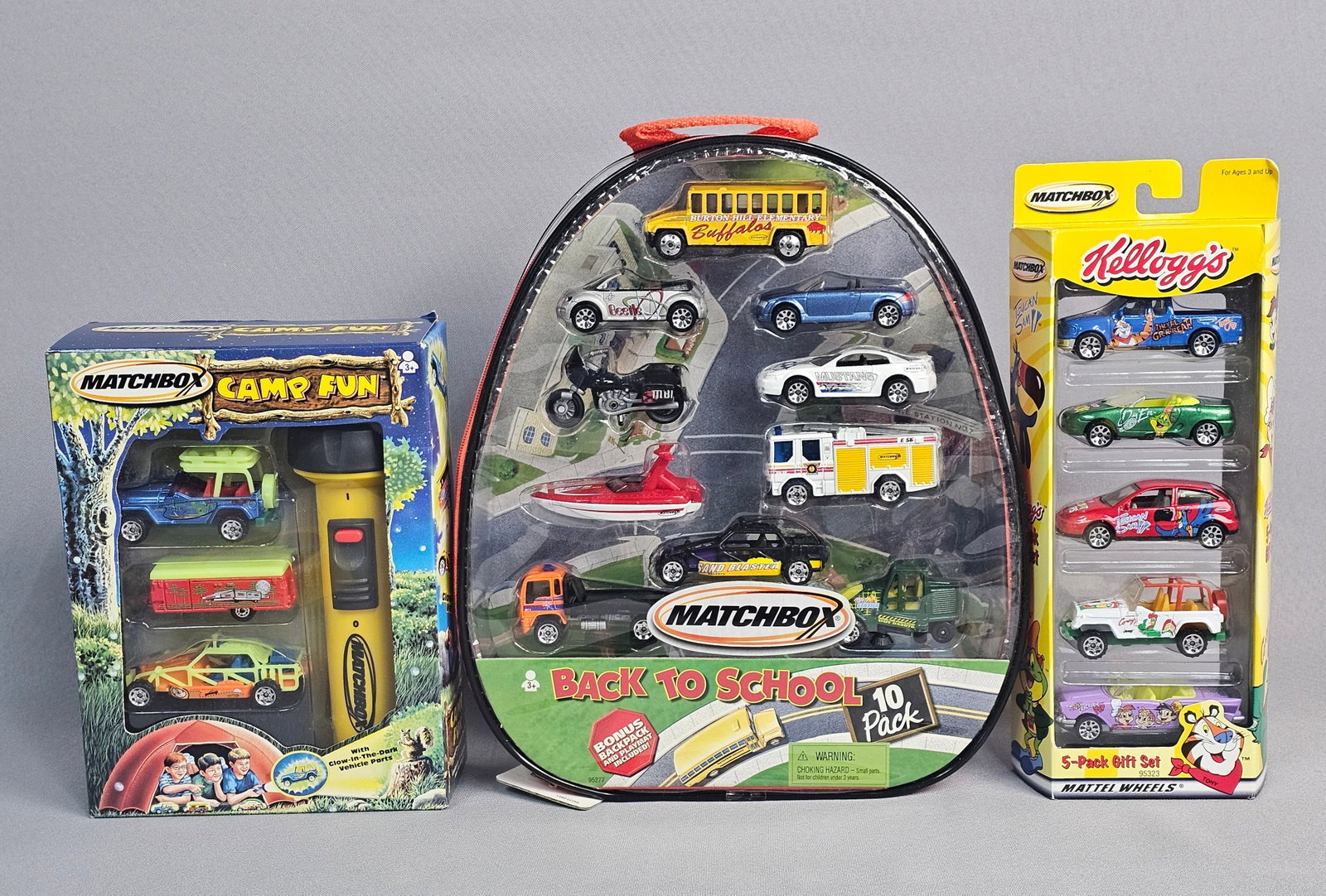 Three Matchbox Vehicle Sets in Boxes: A collection of three Matchbox vehicle sets manufactured by Mattel, Inc., all contained within their original factory packaging. Each set consists of die-cast metal and plastic components. The first s