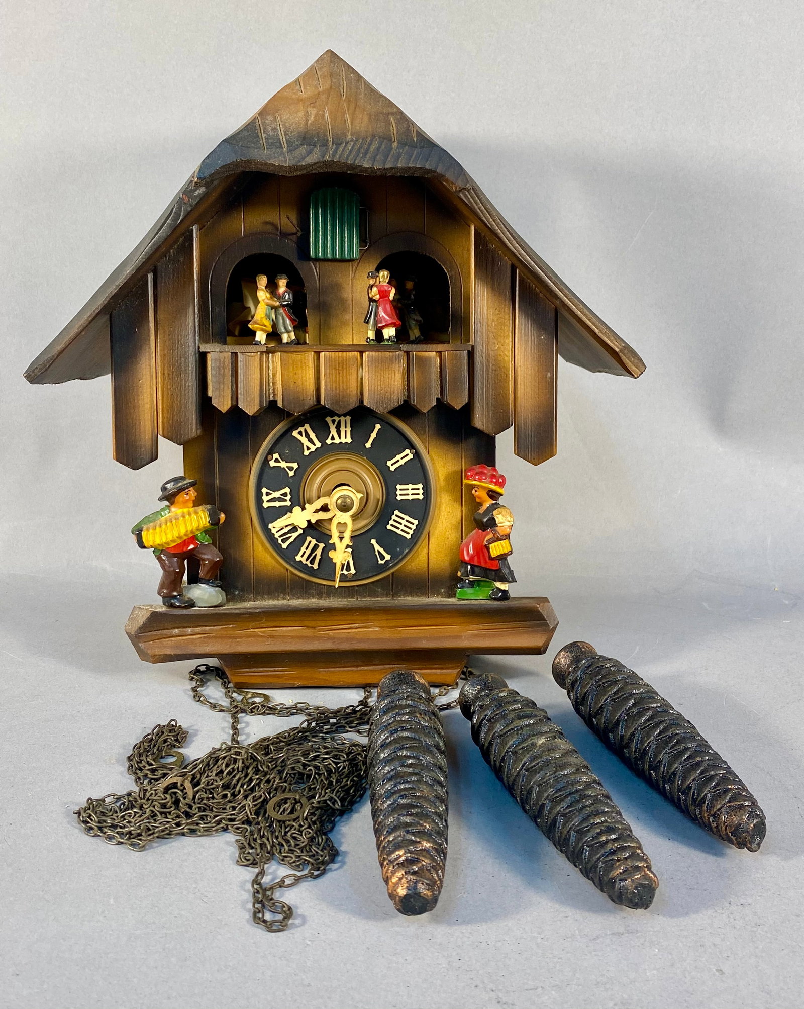 West German Chalet Style Musical Cuckoo Clock: A vintage chalet-style musical cuckoo clock featuring a mechanical weight-driven movement. The carved wood case is decorated with hand-painted figures including four rotating dancers on an upper balco