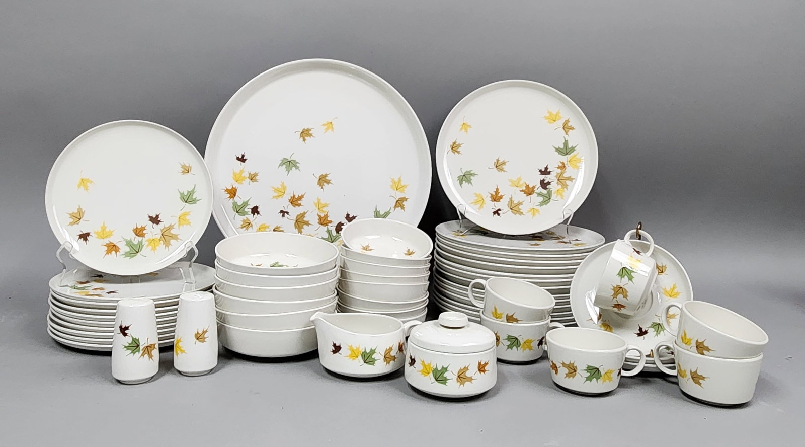 Franciscan Indian Summer Dinnerware: This collection of mid-century ceramic dinnerware is produced by Franciscan in the Indian Summer pattern. The design features a motif of scattered autumn leaves in shades of yellow, green, and brown s