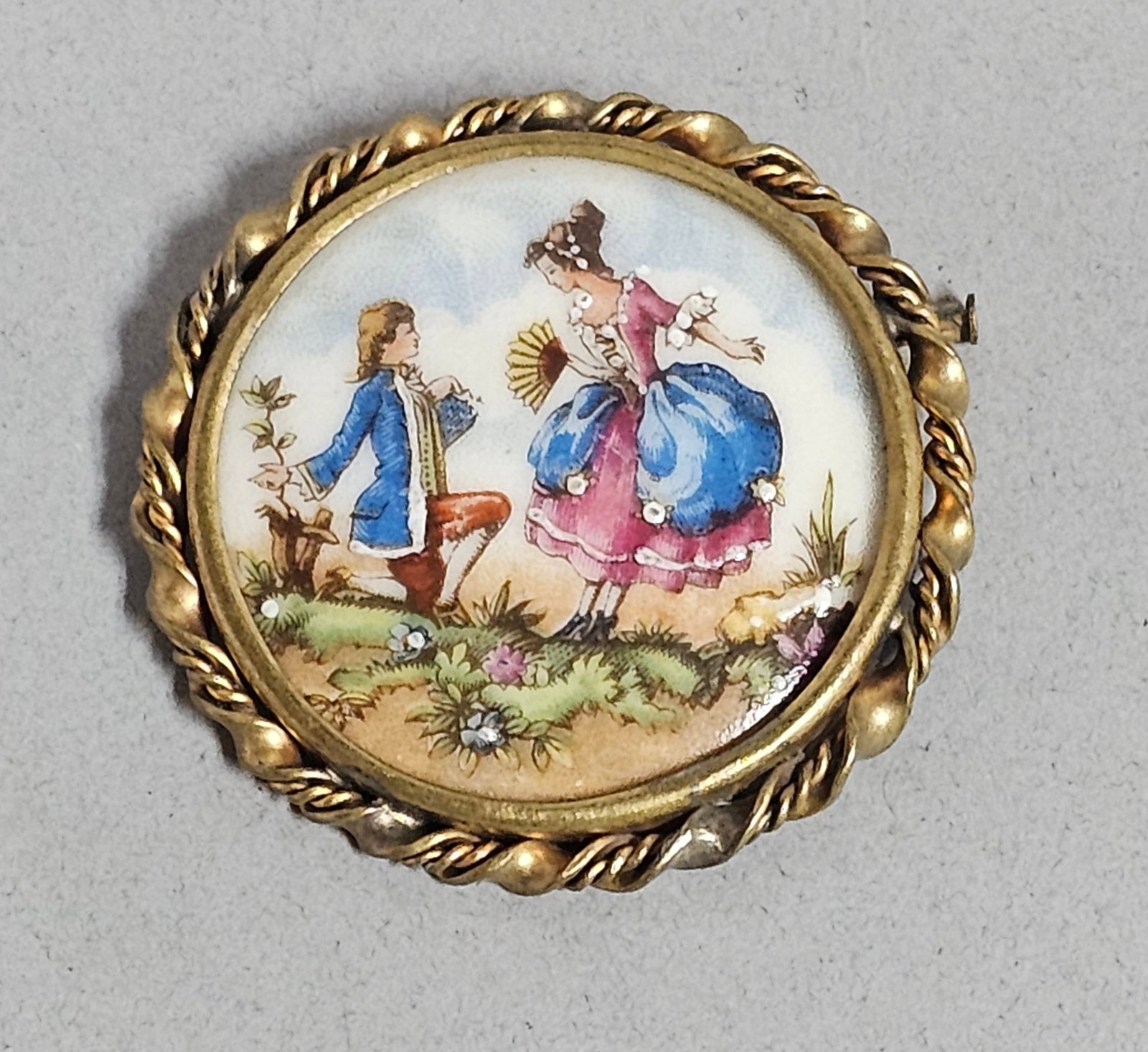 Limoges Porcelain Hand Painted Couple Brooch: A circular porcelain brooch featuring a hand-painted miniature scene in the 18th-century style of a f??te galante. The brooch is equipped with a pin stem and a rotating safety clasp. Diameter: 1.5 inc