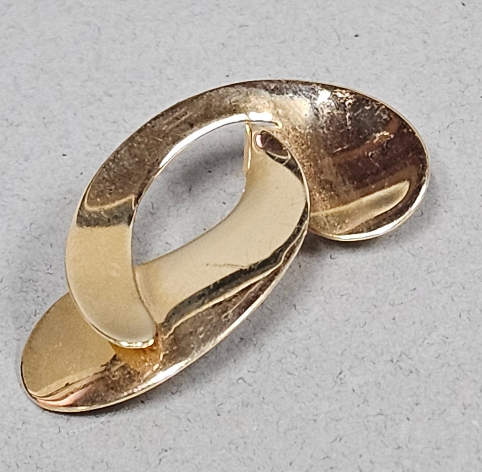 14K Gold Abstract Ribbon Brooch 3.4 Grams: A modern, abstract brooch crafted in 14 karat yellow gold, featuring a polished, fluid ribbon design. The piece is constructed with a standard pin stem and a safety catch on the reverse. Weight: 3.4 g
