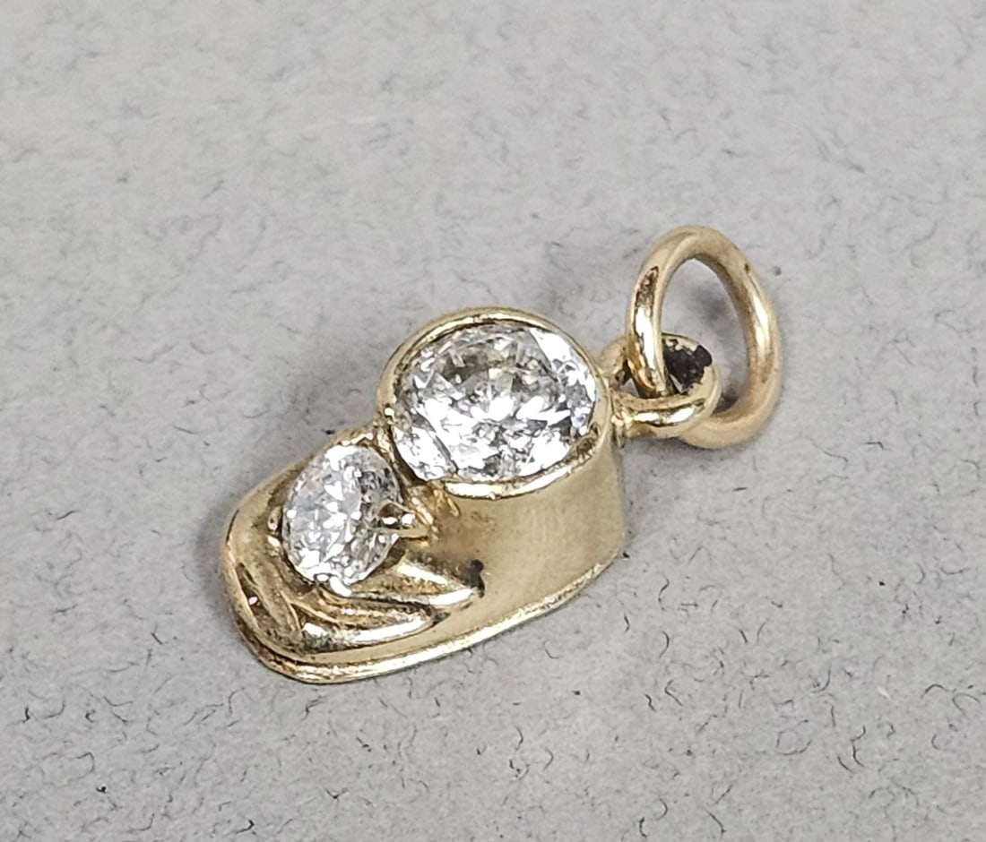10K Baby Shoe Charm with Clear Stones 1.4 Grams: A 10 karat yellow gold charm designed in the form of a baby shoe. The piece is set with two round brilliant-cut clear stones. Weight: 1.4 grams Length: 0.5 inches. The charm exhibits minor surface wea