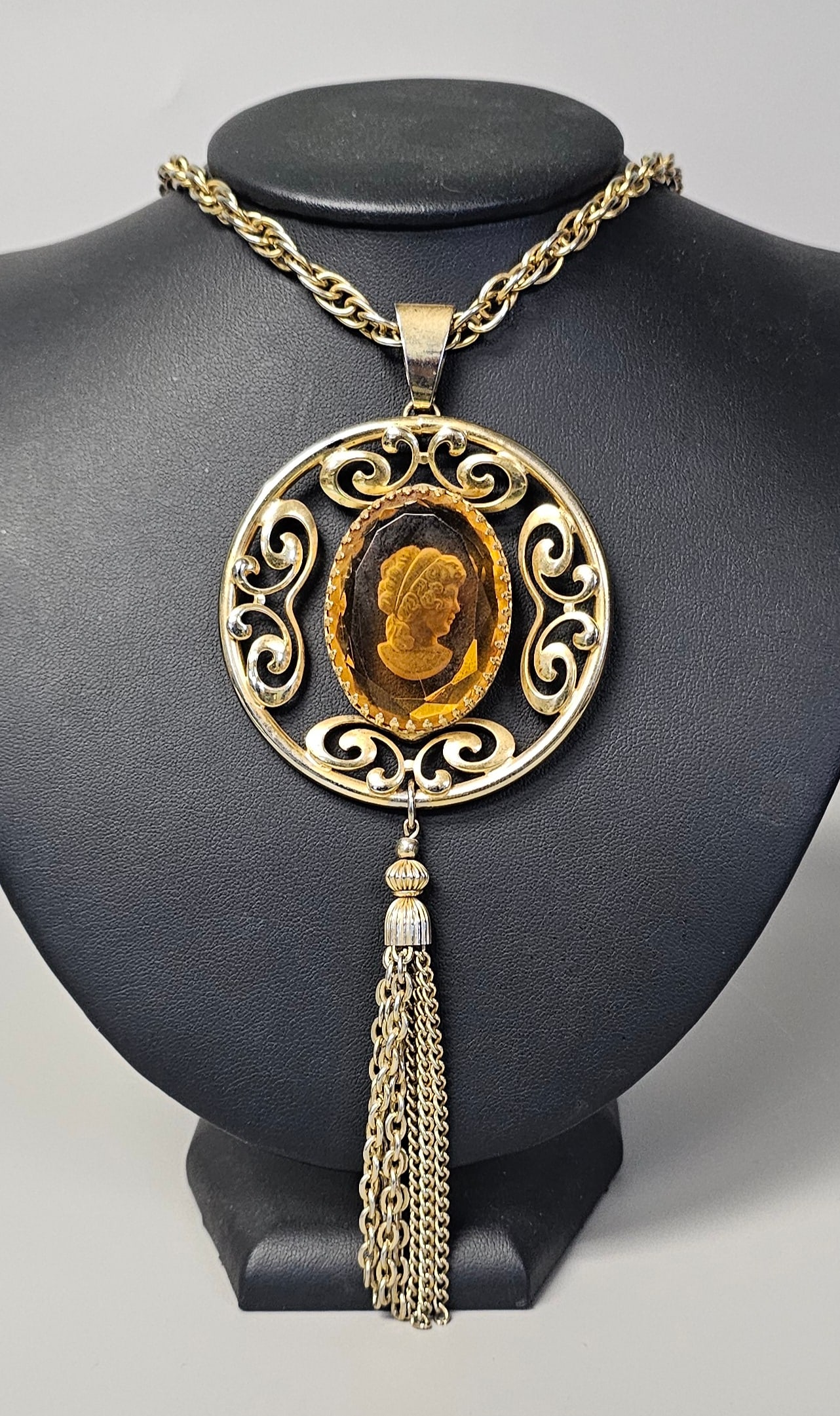 1960s Intaglio Cameo Necklace: A gold-tone costume jewelry necklace featuring an openwork pendant with an amber-colored intaglio cameo and a multi-chain tassel, measuring approximately 36 inches in total length. Good vintage condit