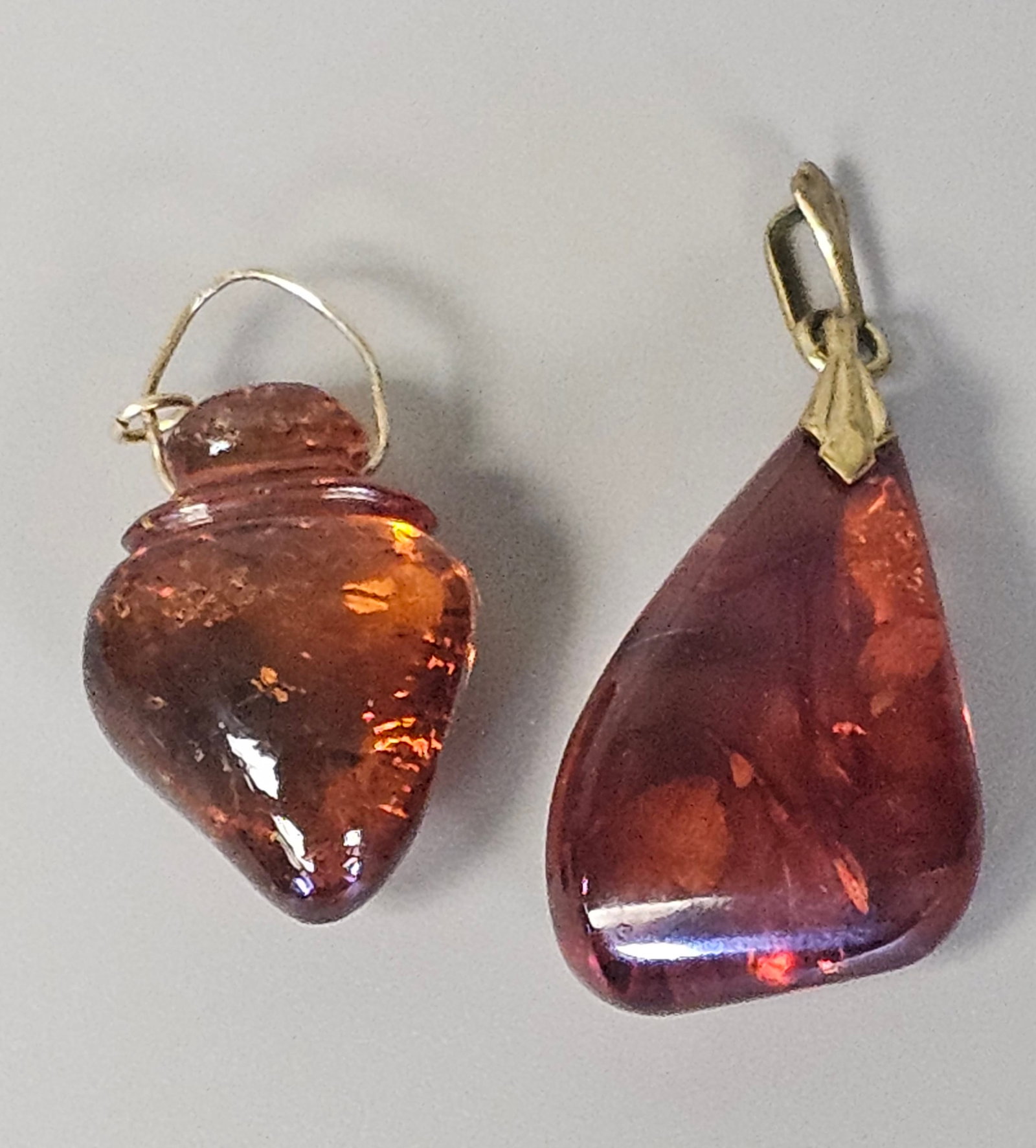 Two Translucent Cognac Amber Pendants: This lot features two individual pendants crafted from translucent cognac-colored amber. The smaller pendant is carved in a form reminiscent of an amphora or vessel, featuring a horizontally ribbed ne