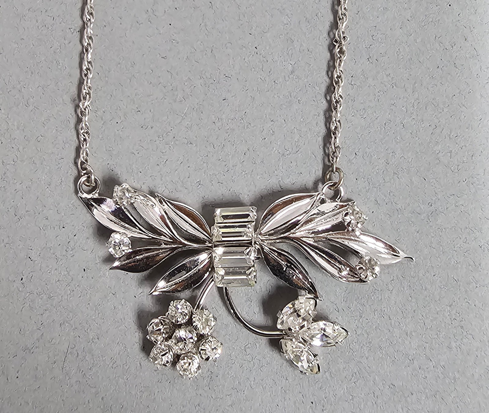 Crown Marie Sterling & Rhinestone Necklace 6.3 Grams: This vintage necklace features a sterling silver centerpiece designed as a stylized bow with floral and leaf motifs. Length: 14 inches Weight: 6.3 grams The necklace is in good vintage condition. Tarn