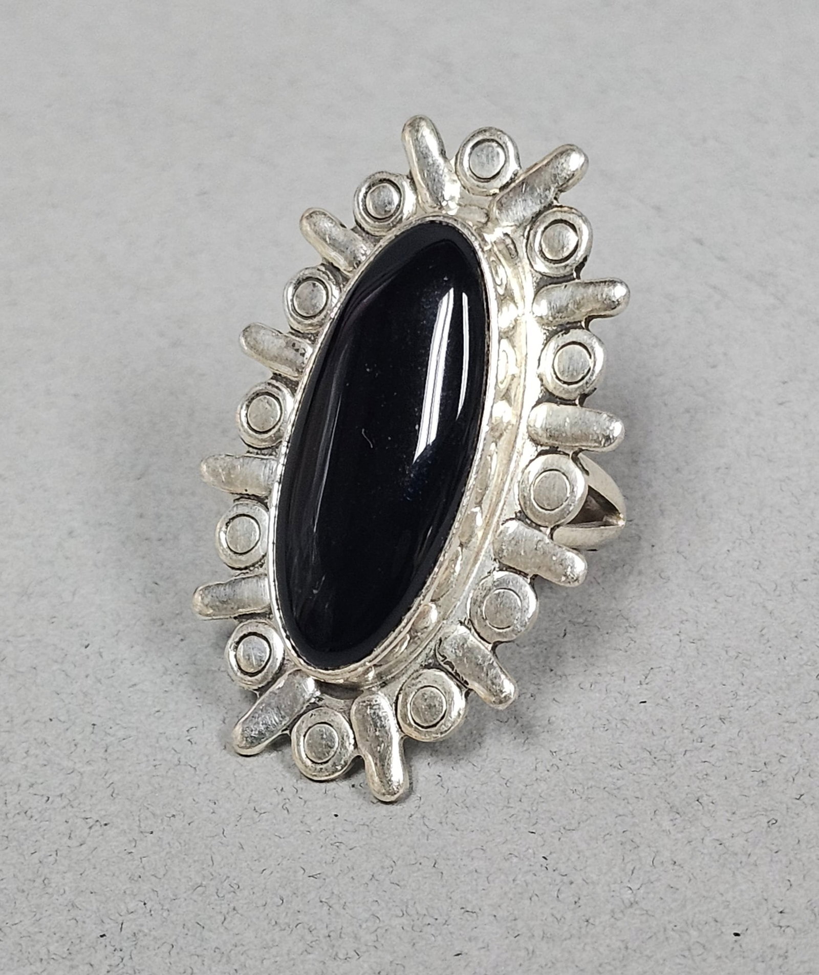Mexican Sterling Black Onyx Sunburst Ring 12.6 Grams: A Mexican sterling silver modernist-style cocktail ring. The piece features a central oval black onyx cabochon stone secured in a bezel setting. Ring size: 6 Total weight: 12.6 grams Ring face