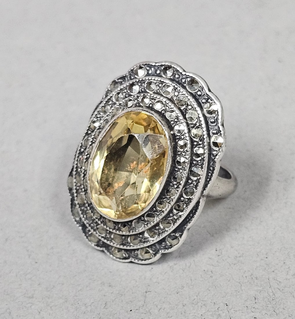 Sterling Marcasite & Yellow Gemstone Ring 7.6 Grams: A vintage-style tiered cocktail ring crafted from sterling silver The ring features a prominent bezel-set oval faceted light-yellow gemstone, resembling citrine, at its center. This central stone is f