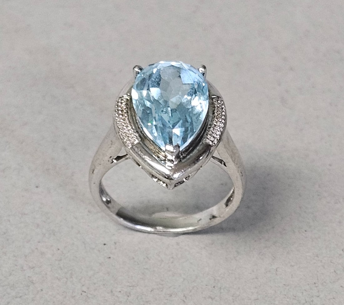 Sterling Silver Blue Topaz Style Ring: This cocktail ring is crafted from sterling silver and features a large pear-cut light blue gemstone at its center. The gemstone displays characteristics consistent with blue topaz. The interior of th