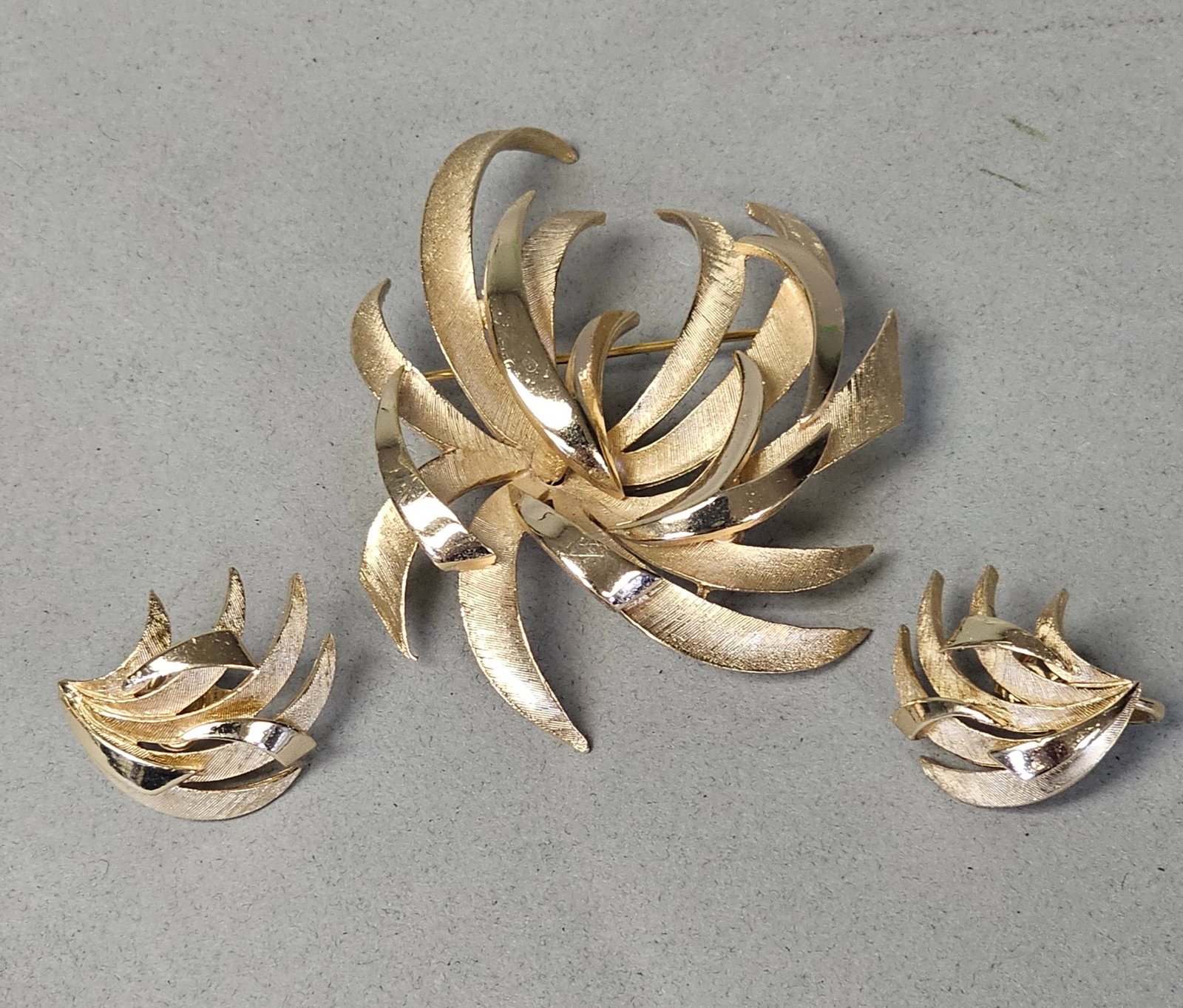 Crown Trifari Gold-Tone Fireworks Jewelry Set: This vintage costume jewelry set is a matching suite by Trifari. The set consists of one brooch and one pair of clip-on earrings. The design features a stylized abstract fireworks or sunburst motif cr