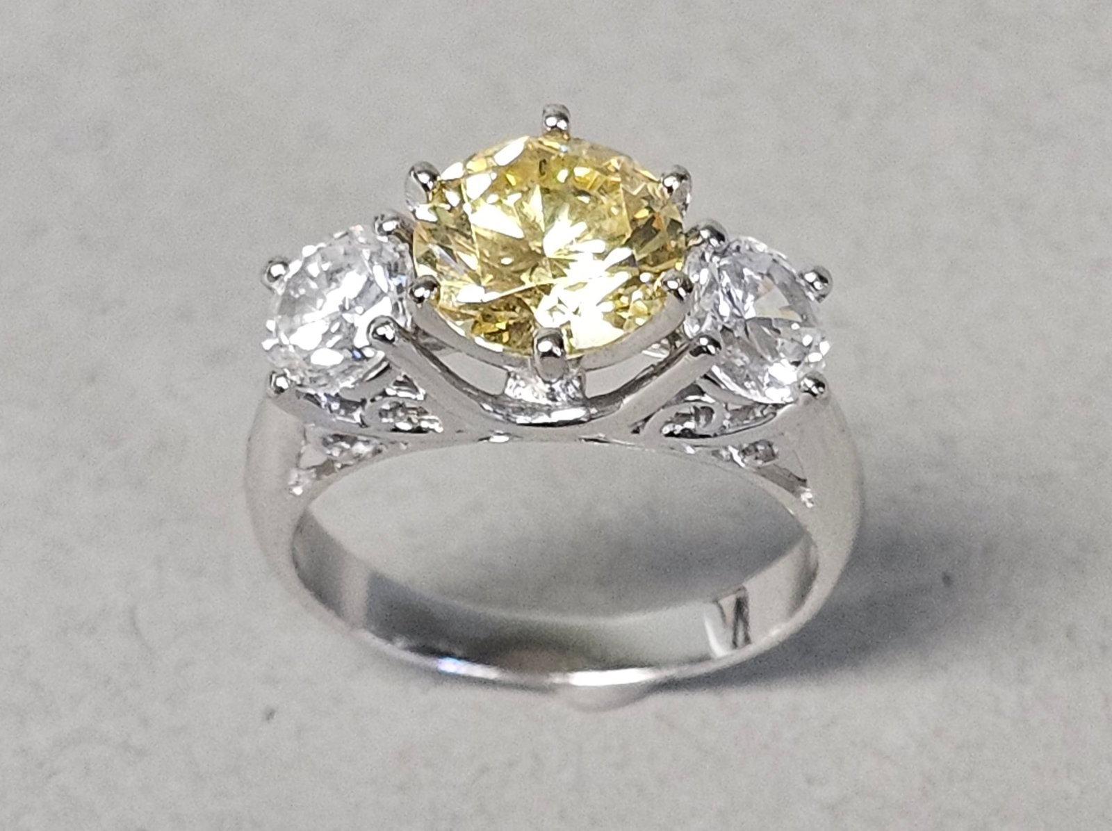 Sterling Ring with Yellow & Colorless Stones 4.0 Grams: A three-stone ring crafted from sterling silver. The design features a large round brilliant-cut canary yellow-colored stone as the centerpiece, secured in a six-prong setting. This central stone is f