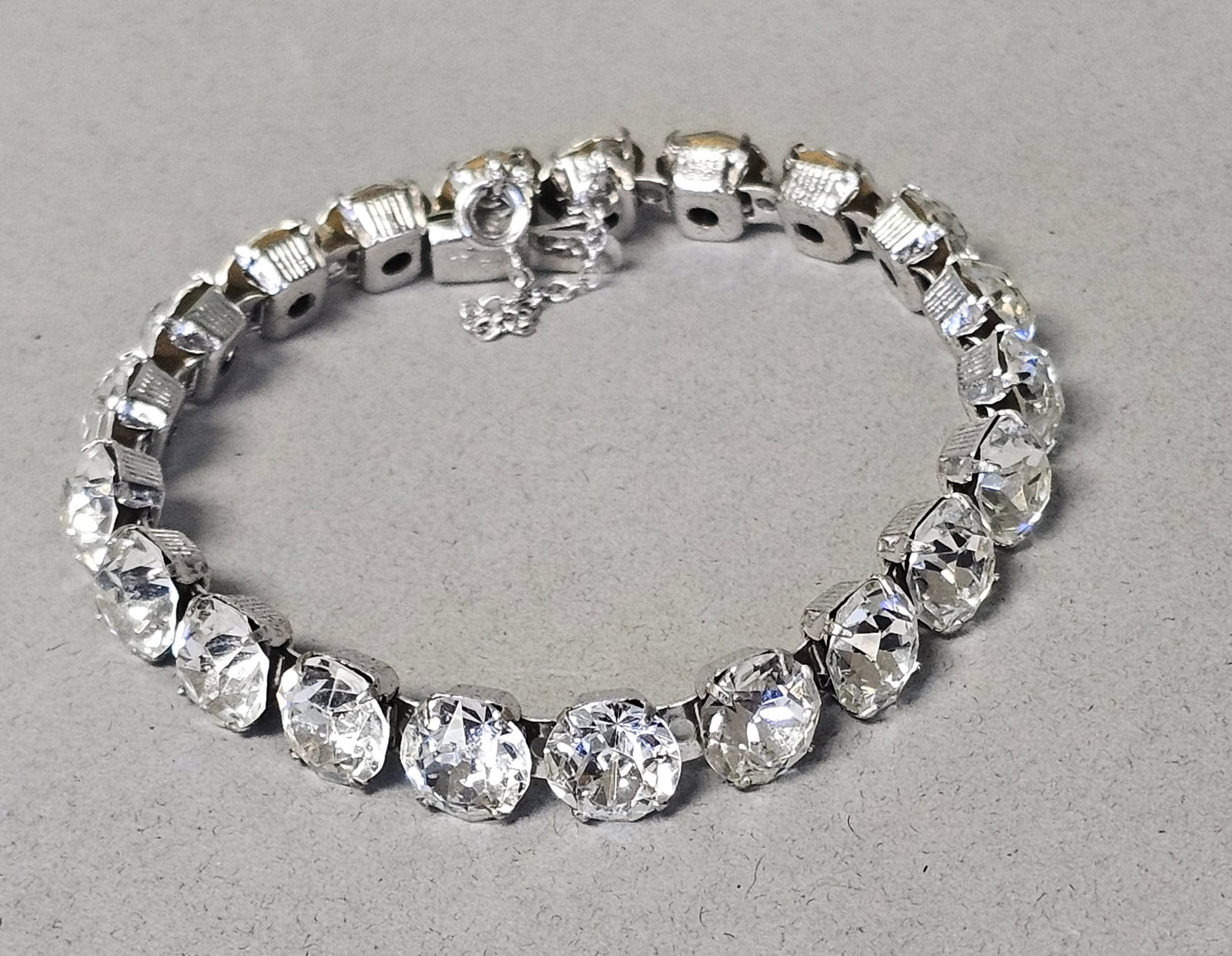 Eisenberg Ice Silver-Tone Clear Rhinestone Bracelet: This is a vintage costume jewelry line bracelet in the tennis style by Eisenberg. The bracelet is composed of silver-tone metal and set with a single row of round-cut clear glass rhinestones. Each rhi