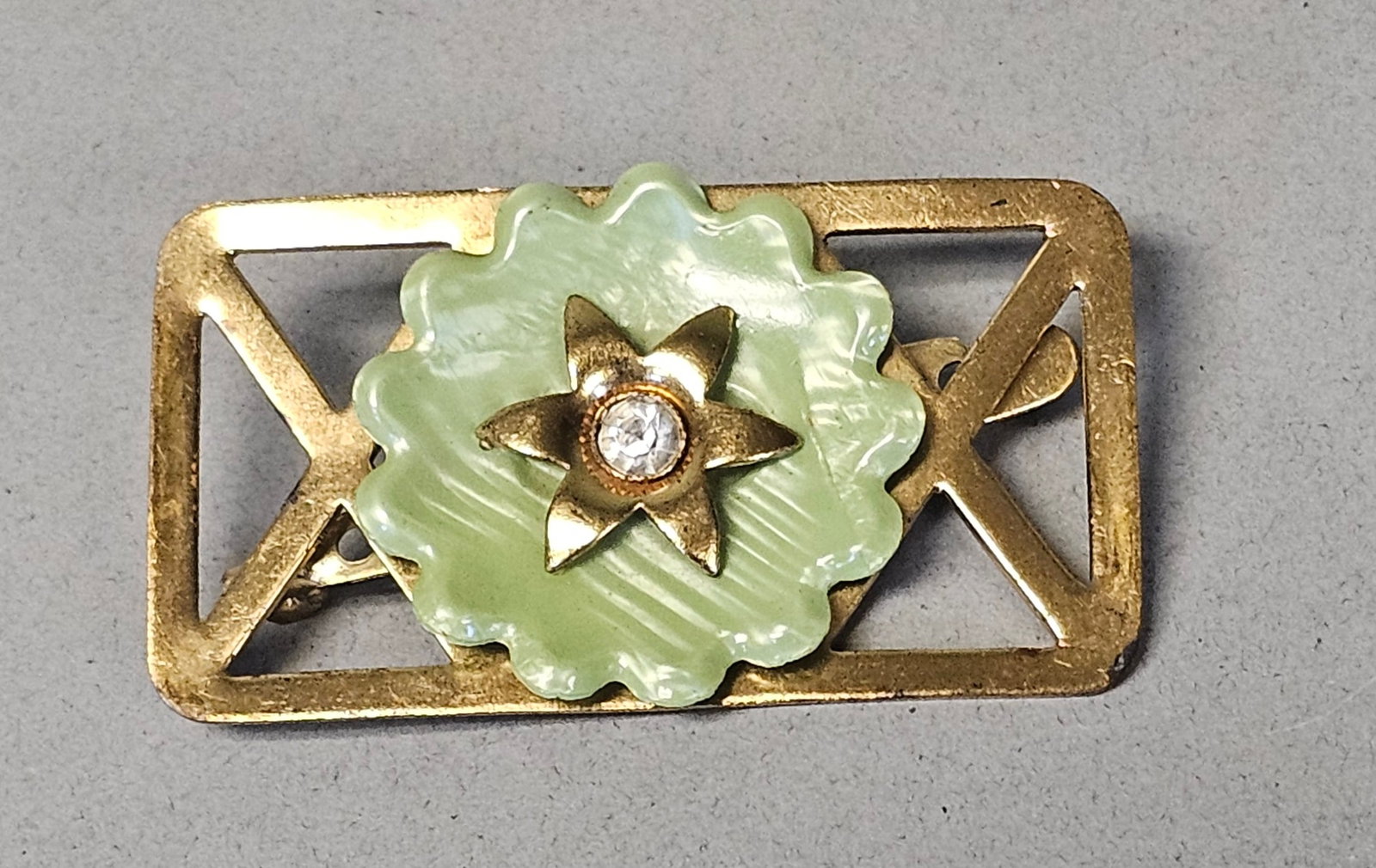 Mid-Century Green Molded Plastic Bar Brooch: A vintage rectangular bar brooch from the mid-20th century featuring a central floral motif. The focal point is a scalloped, pale mint-green molded plastic disc with decorative radiating ridges. The
