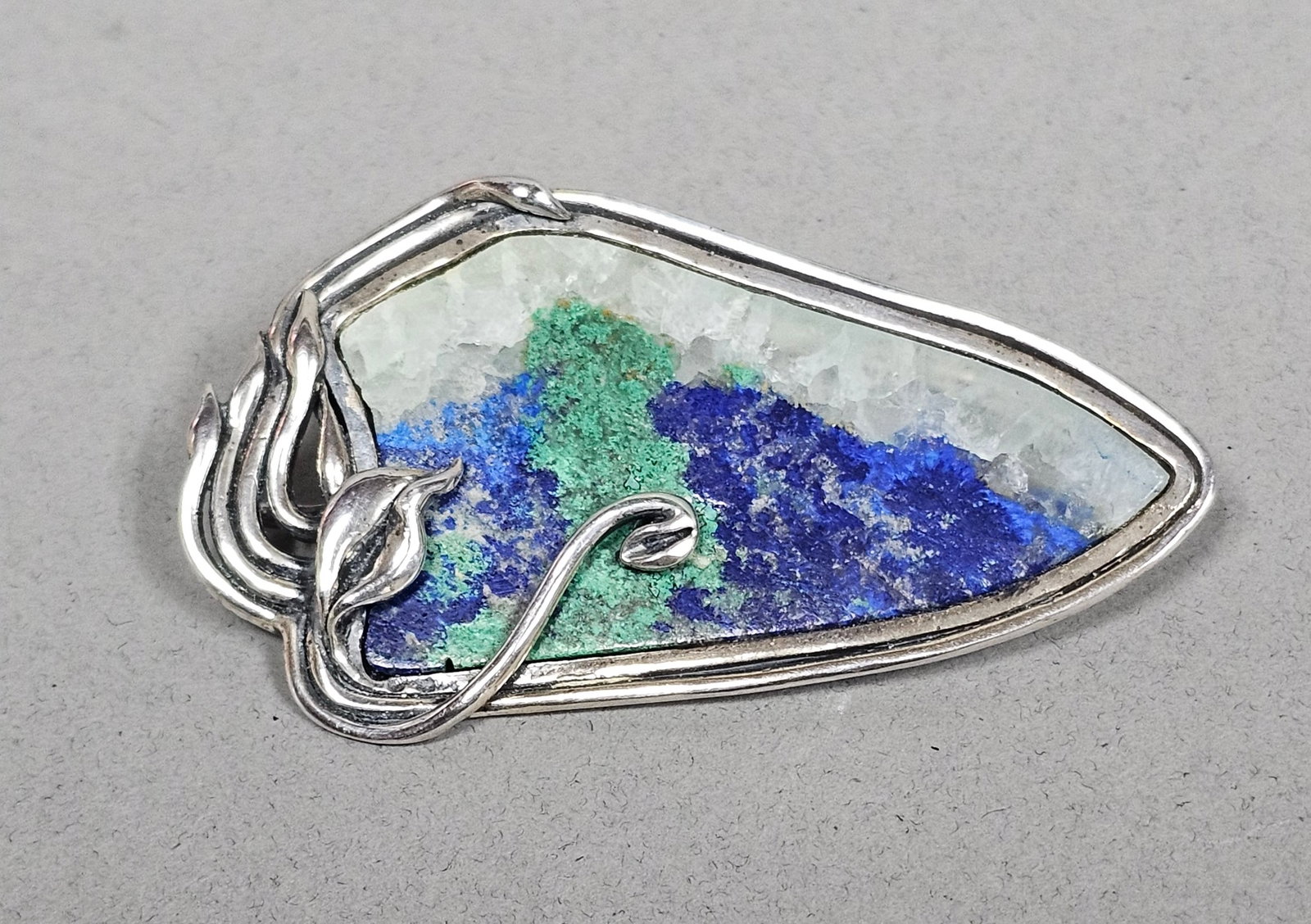 Sterling Azurite & Malachite Matrix Brooch 21.2 Grams: This item is an Art Nouveau style brooch pendant crafted in sterling silver. The setting features an organic design of flowing vines and stylized leaves that gracefully frame a large, asymmetrical, po