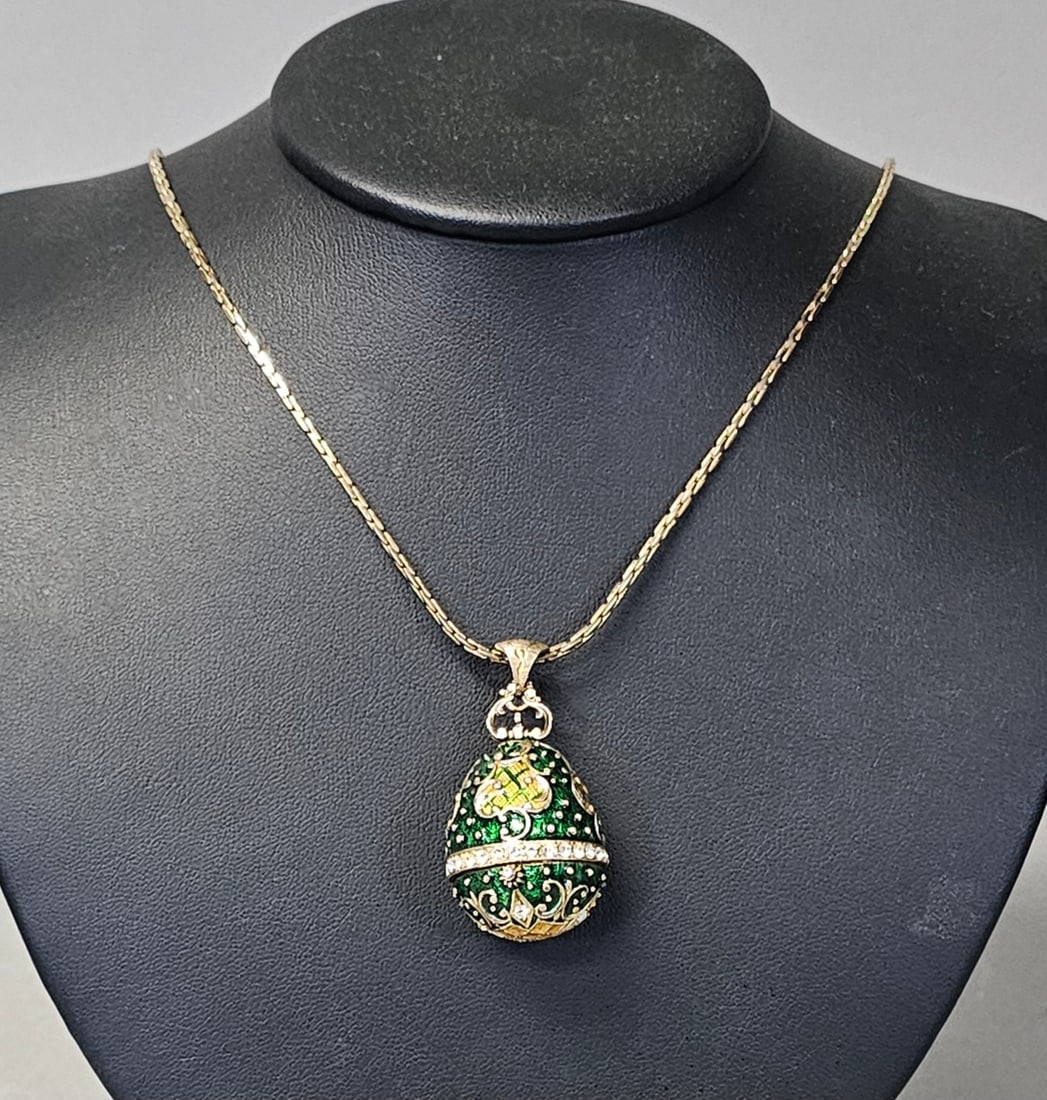 Park Lane Enamel Hinged Egg Pendant Necklace: A costume jewelry pendant necklace by Park Lane featuring a Russian-style hinged egg. The gold-tone metal pendant is decorated with green and yellow enamel scrollwork and filigree, accented with a cen