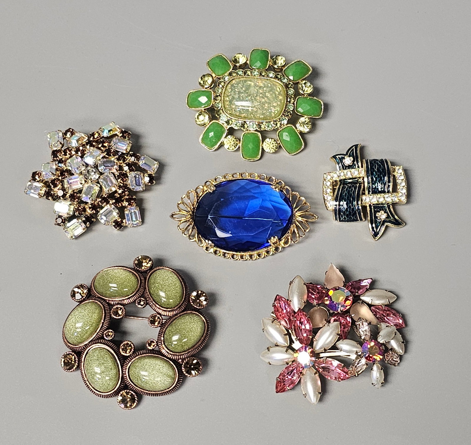 Costume Jewelry Brooches Inc St. John: This lot features an assortment of six costume jewelry brooches in various styles and materials. One brooch is a stylized bow or interlaced ribbon design finished with textured black enamel and small 