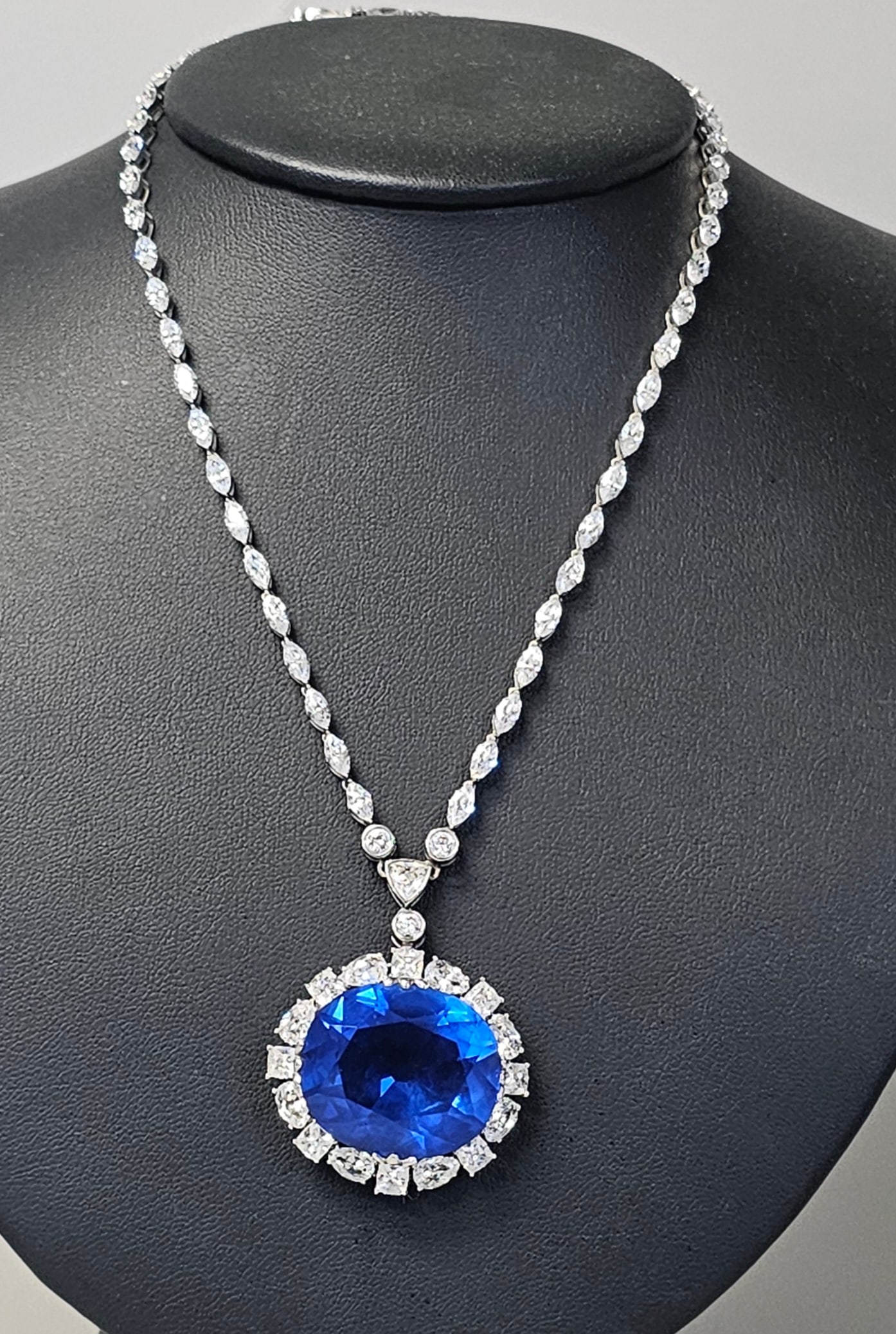 Smithsonian Simulated Hope Diamond Necklace: A silver-toned statement necklace featuring a gemstone line chain and a large oval-cut pendant. The chain is composed of linked marquise-cut and round-cut clear synthetic stones. The pendant features 