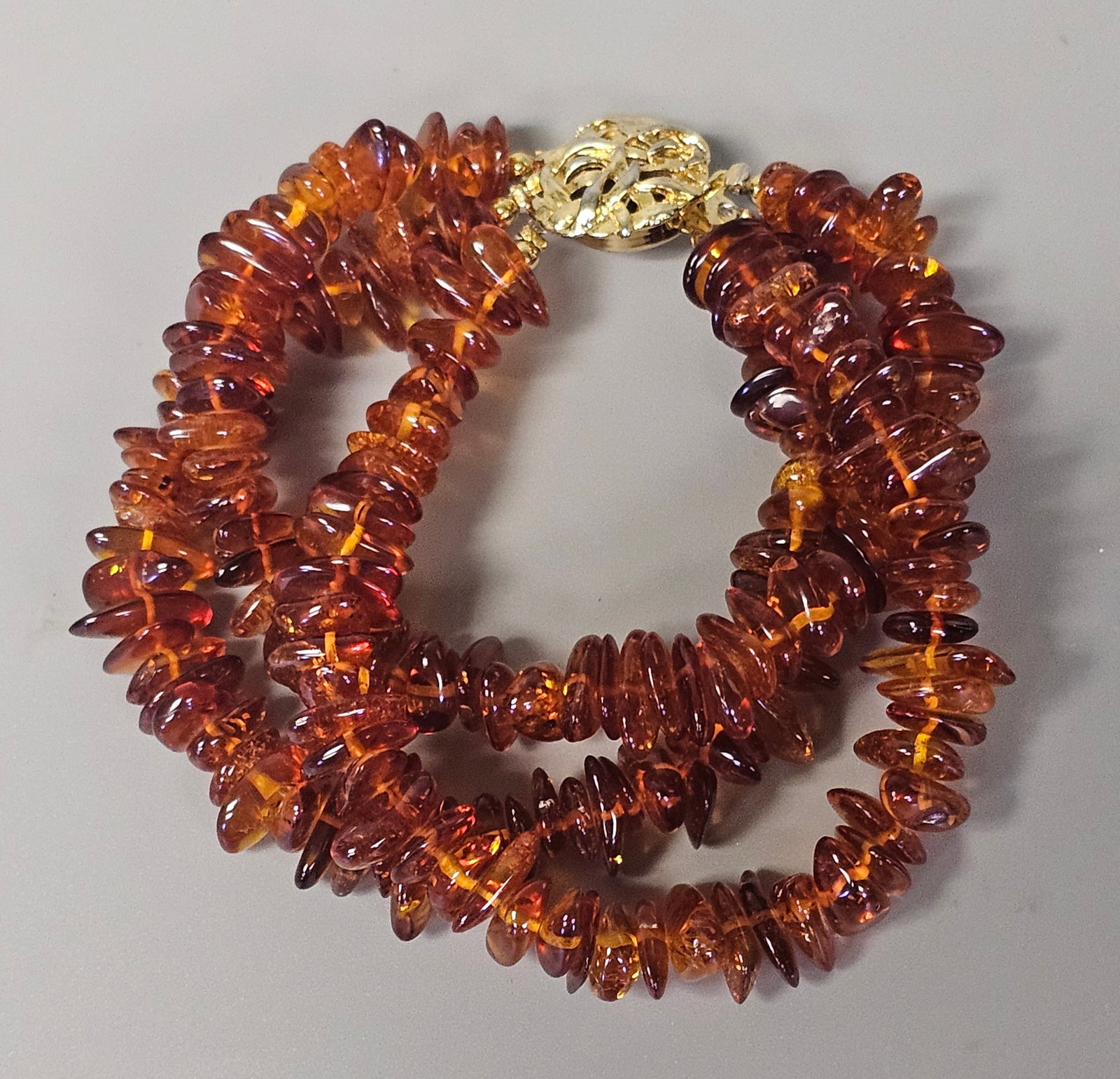 Three-Strand Tumbled Amber Bracelet: Attributed to Baltic amber, this three-strand bracelet is composed of polished, irregular amber nuggets in a variety of natural tones, ranging from light honey to deep reddish-cognac. The amber