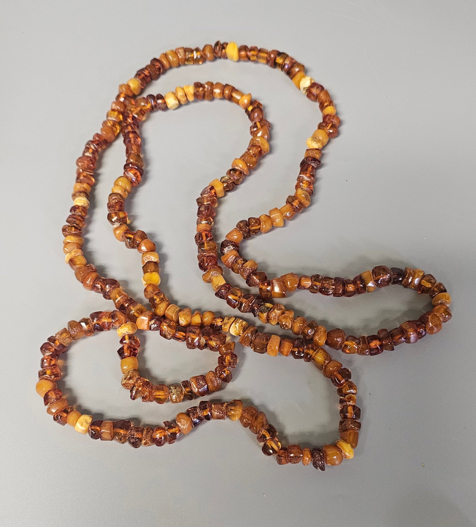Opera Length Tumbled Amber Bead Necklace: This lot consists of a single, exceptionally long continuous strand of beads composed of natural amber. The beads are shaped into irregular, tumbled chips and small nuggets, displaying a variety of