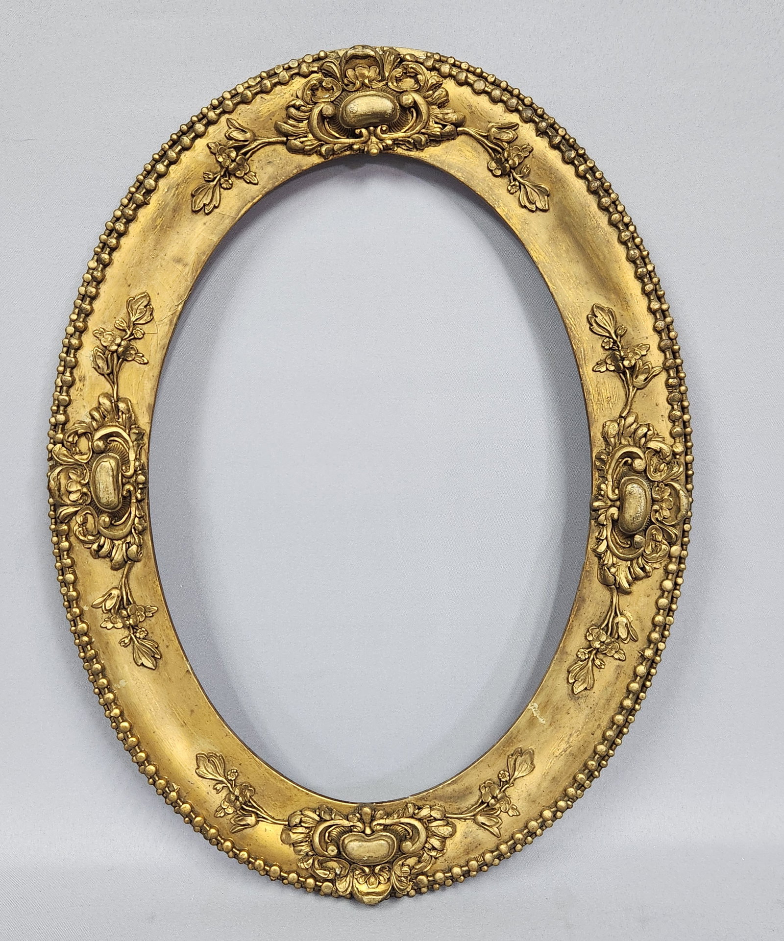 19th Century Neoclassical Frame: A decorative oval frame in the Neoclassical or Louis XVI revival style, featuring a core structure of segmented wood with applied composition ornamentation. Approximate outer width: 14 inches