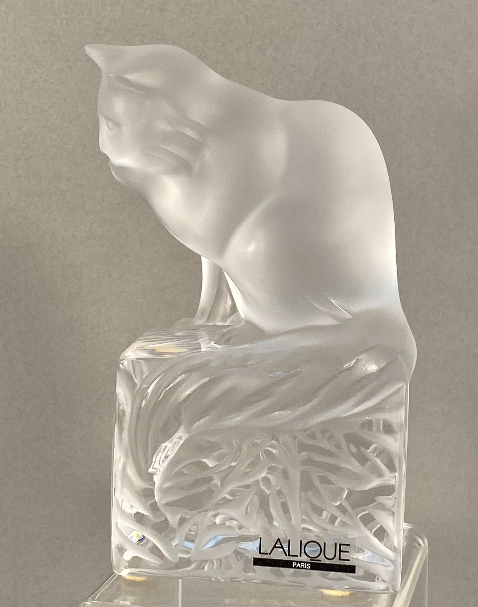 Lalique Frosted & Clear Crystal Cat Figurine: A Lalique crystal figurine depicting a cat in a grooming pose perched on a square pedestal base. The feline figure features a signature satin frosted finish and is shown with its head turned, licking