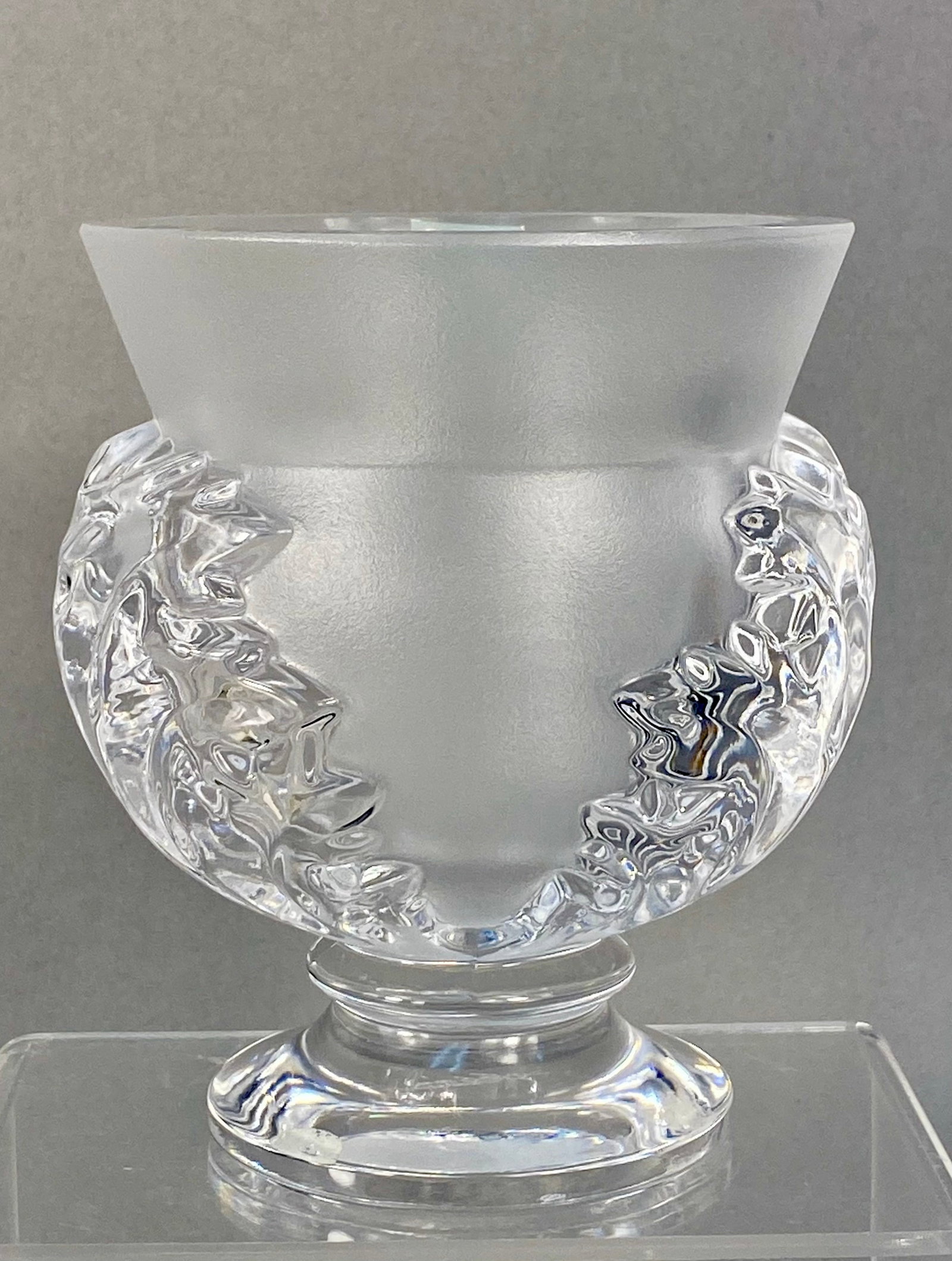 Lalique France Saint-Cloud Crystal Vase: A Lalique crystal pedestal vase in the Saint-Cloud pattern. The vessel features a flared rim and a body of satin-finished frosted crystal. The sides are decorated with high-relief, molded acanthus