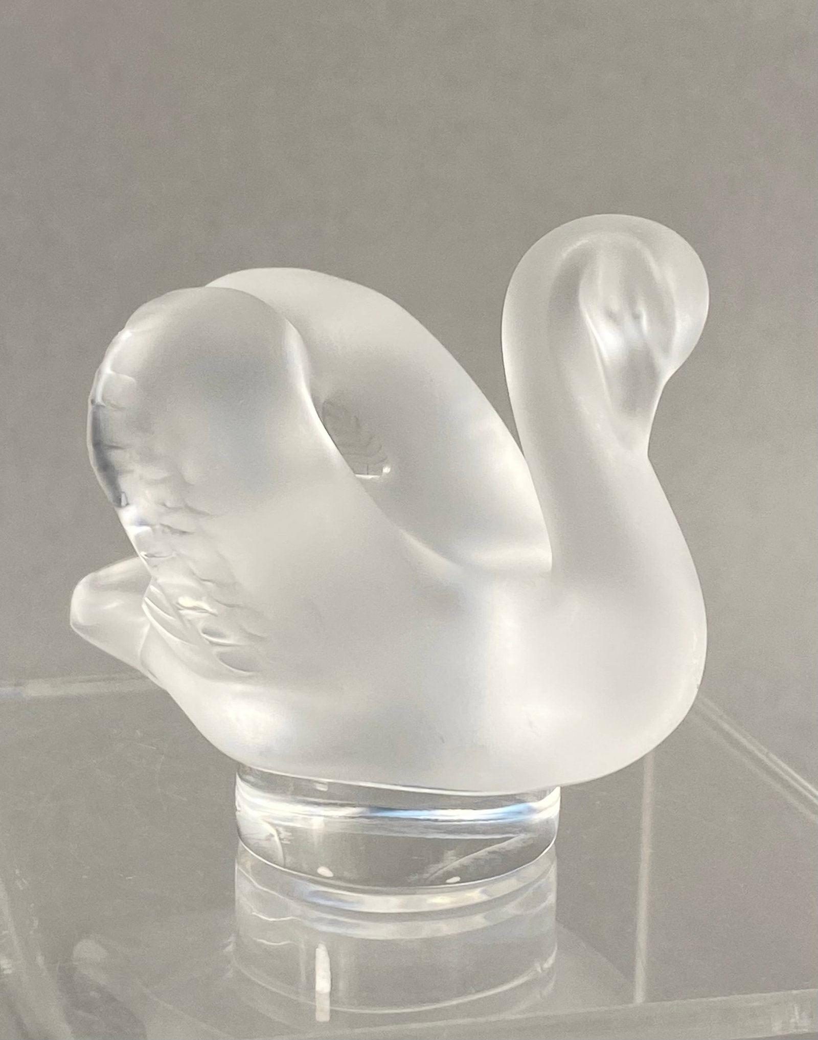 Lalique France Crystal Cygne Swan Figurine: A frosted lead crystal figurine of a swan produced by Lalique France. The figurine depicts a swan in a graceful pose with its neck curved downward and its head tucked toward its chest. The body