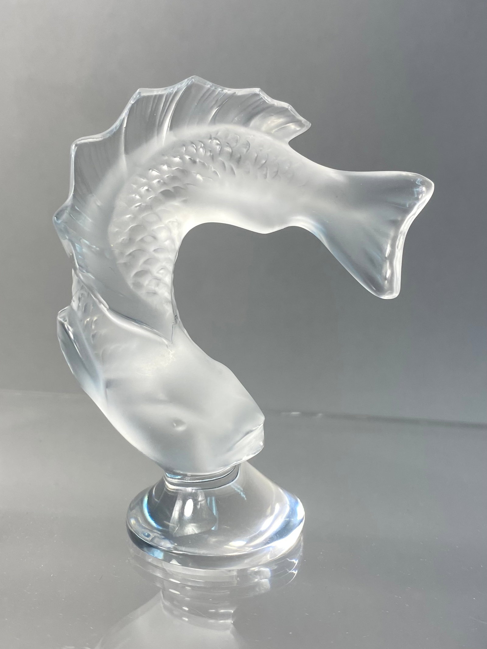 Lalique Goujon Crystal Leaping Fish Figurine: A Lalique crystal figurine titled Goujon, depicting a leaping fish in a dynamic arched pose. The body of the fish is rendered in frosted glass, featuring detailed molded scales and prominent fins. The