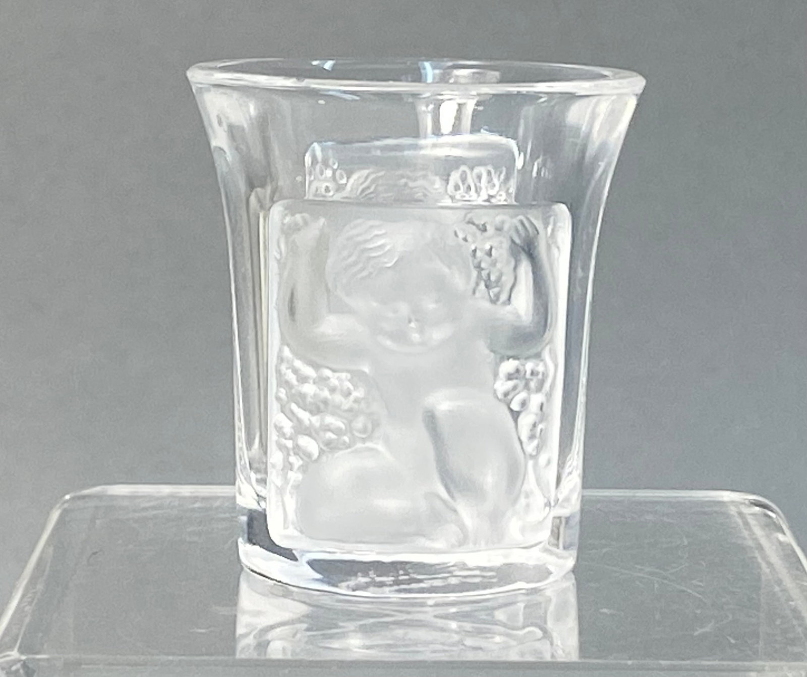 Lalique France Les Enfants Crystal Shot Glass: A crystal shot glass manufactured by Lalique, France, in the Enfants pattern. The vessel is constructed of clear and frosted crystal. The exterior features four molded relief panels depicting nude put