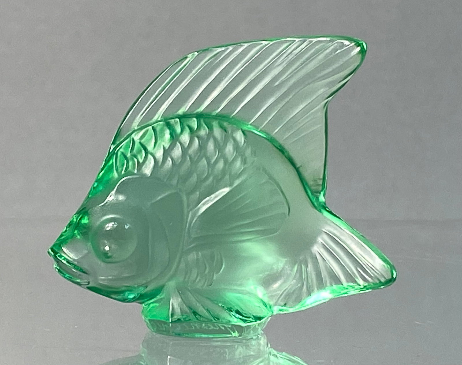 Lalique French Mint Green Glass Poisson Fish Figurine: A Lalique French glass figurine depicting a stylized fish, known as the Poisson model. The piece is crafted from transparent mint green lead crystal. The design features a textured body with molded sc