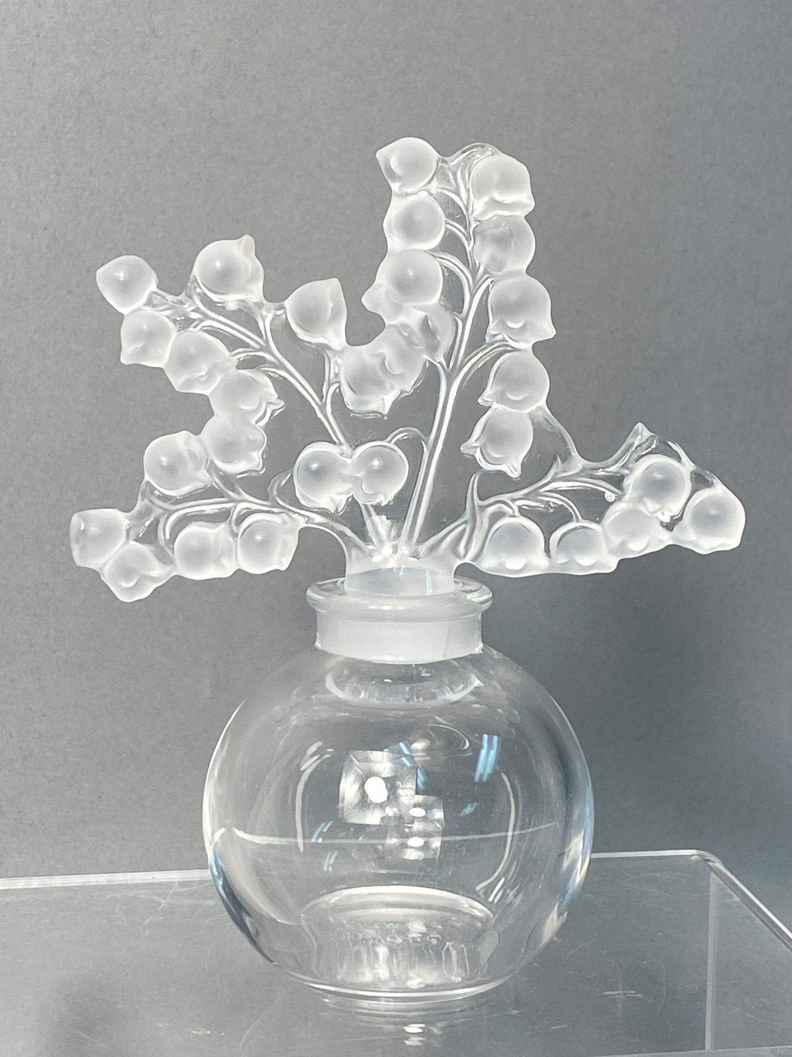 Lalique Clairefontaine Crystal Lily of the Valley Perfume Bottle: This is a Lalique Clairefontaine perfume bottle crafted from French lead crystal. The design features a globular clear glass body paired with an oversized, decorative stopper. The stopper is intricate