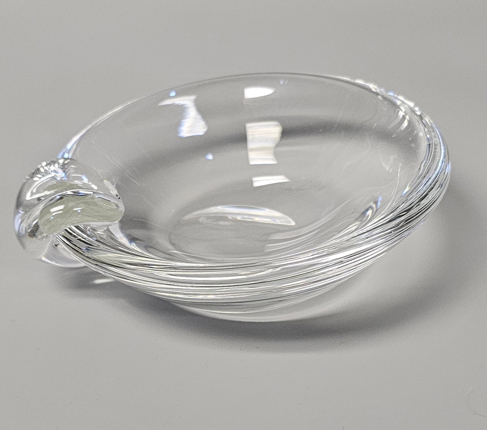 Mid Century Stuben Crystal Ashtray Candy Dish: A hand-blown and hand-formed shallow circular dish crafted from clear crystal by Steuben Glass Works. The vessel features a sloped interior and a thick, rounded rim, accented by a solid glass scrolled