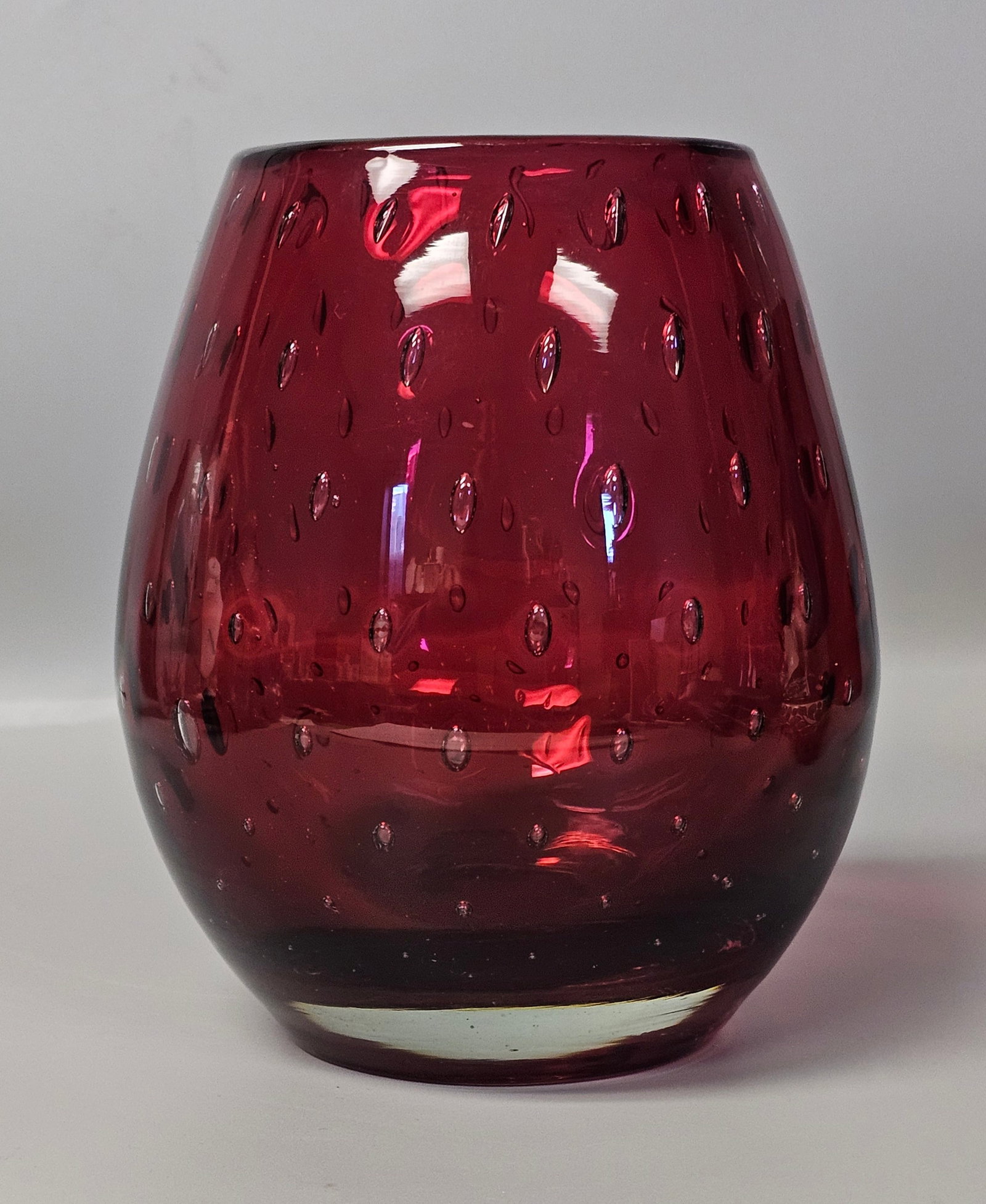 Mid-Century Ruby Red Bullicante Art Glass Vase: A mid-century modern hand-blown art glass vase featuring a tapered, rounded body. The construction utilizes the sommerso technique, with a deep ruby red core encased in a thick layer of clear glass. T
