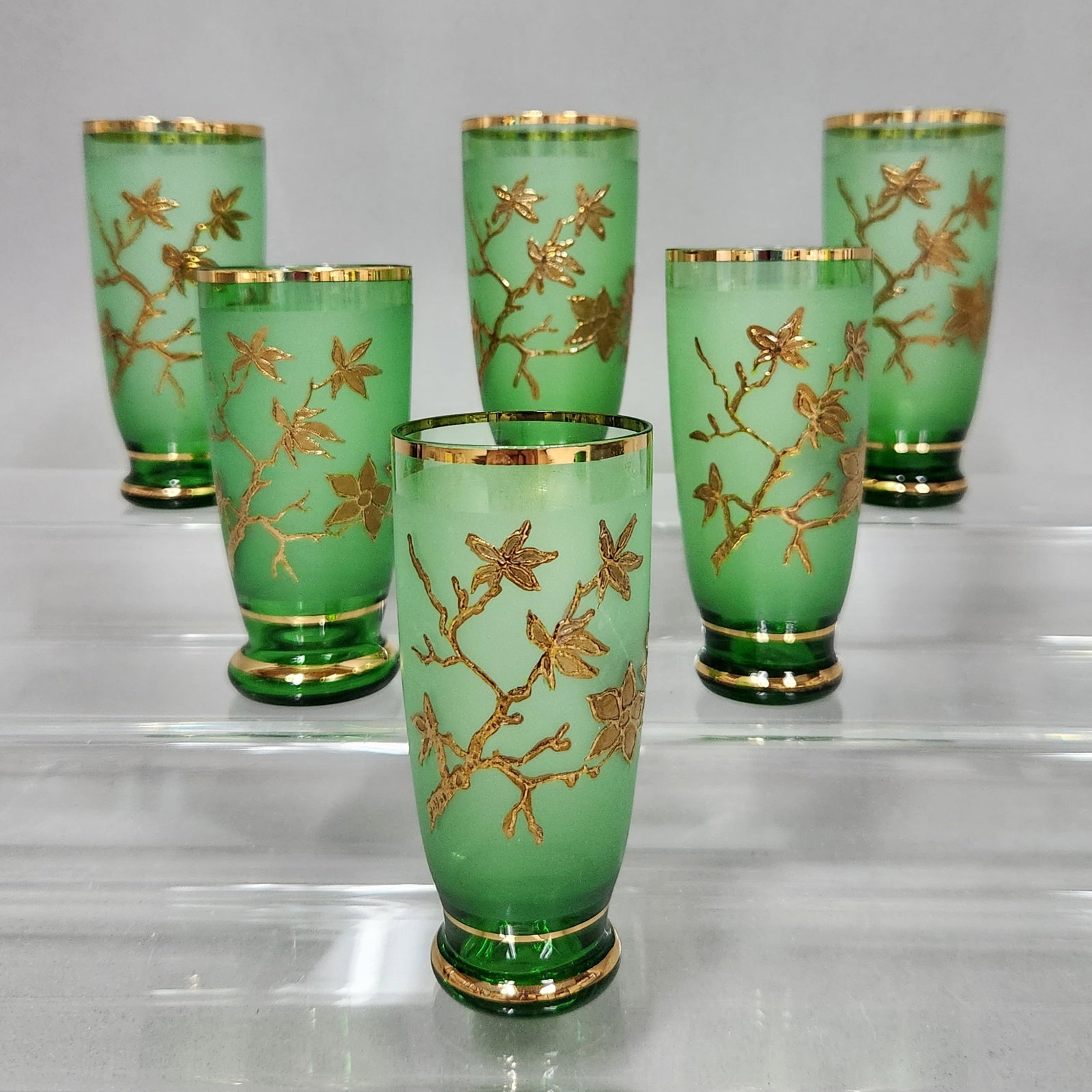 Bohemian Style Green Glass Tumblers: A set of six emerald green glass footed tumblers. Each glass features a slightly tapered form with a pedestal-style base. The central portion of each vessel is finished with a wide, acid-etched froste