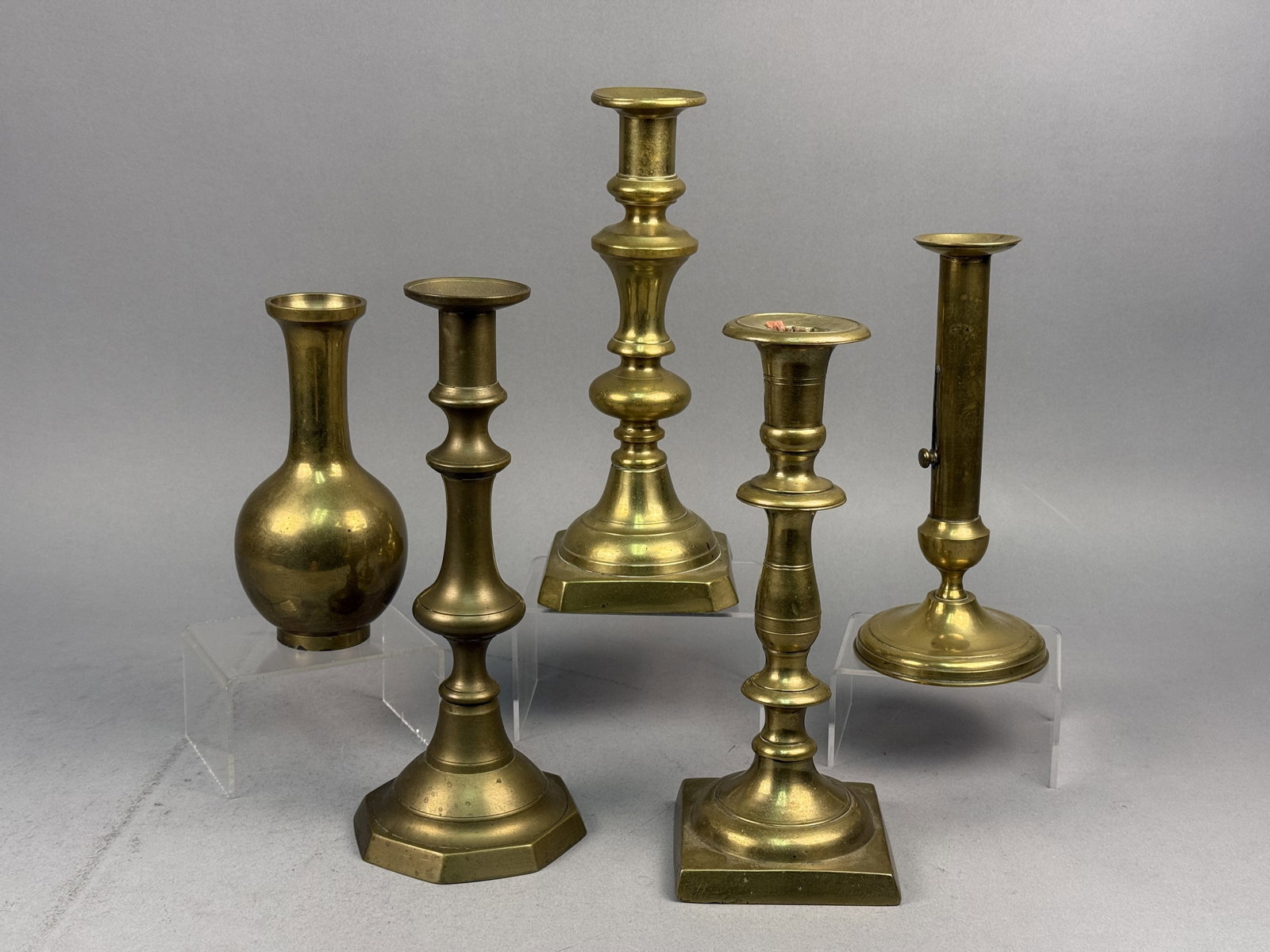Assorted Brass Candlesticks and a Bud Vase: This group of brass decorative items features several candlesticks of varying designs and a bud vase. The assortment includes a candlestick with an octagonal base, two with square bases, and one