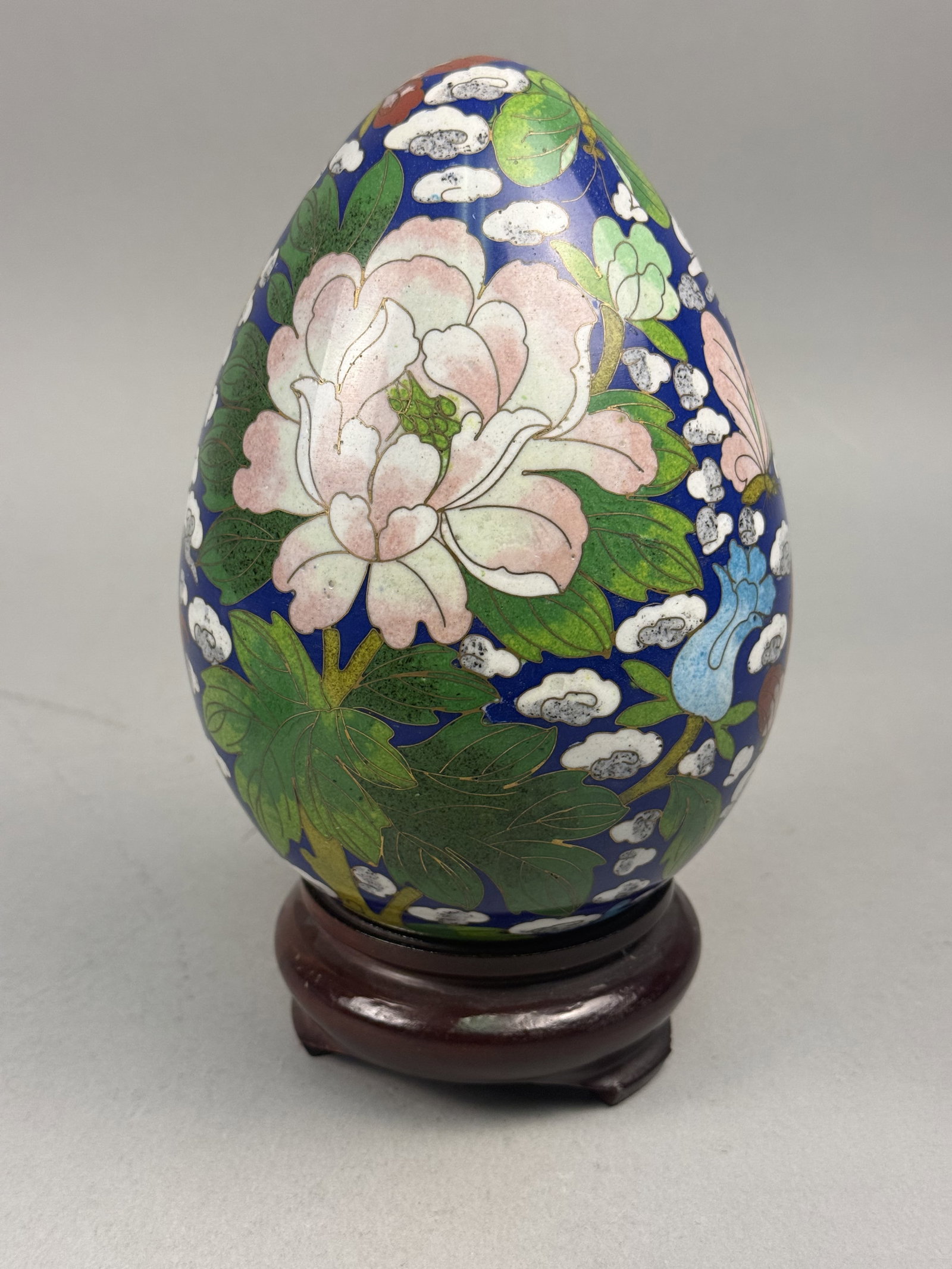 Large Cloisonne Enamel Egg: This large Chinese decorative egg is crafted using the cloisonne technique, featuring brass wires and colored vitreous enamels. The primary motif is a large peony blossom in shades of pink and white